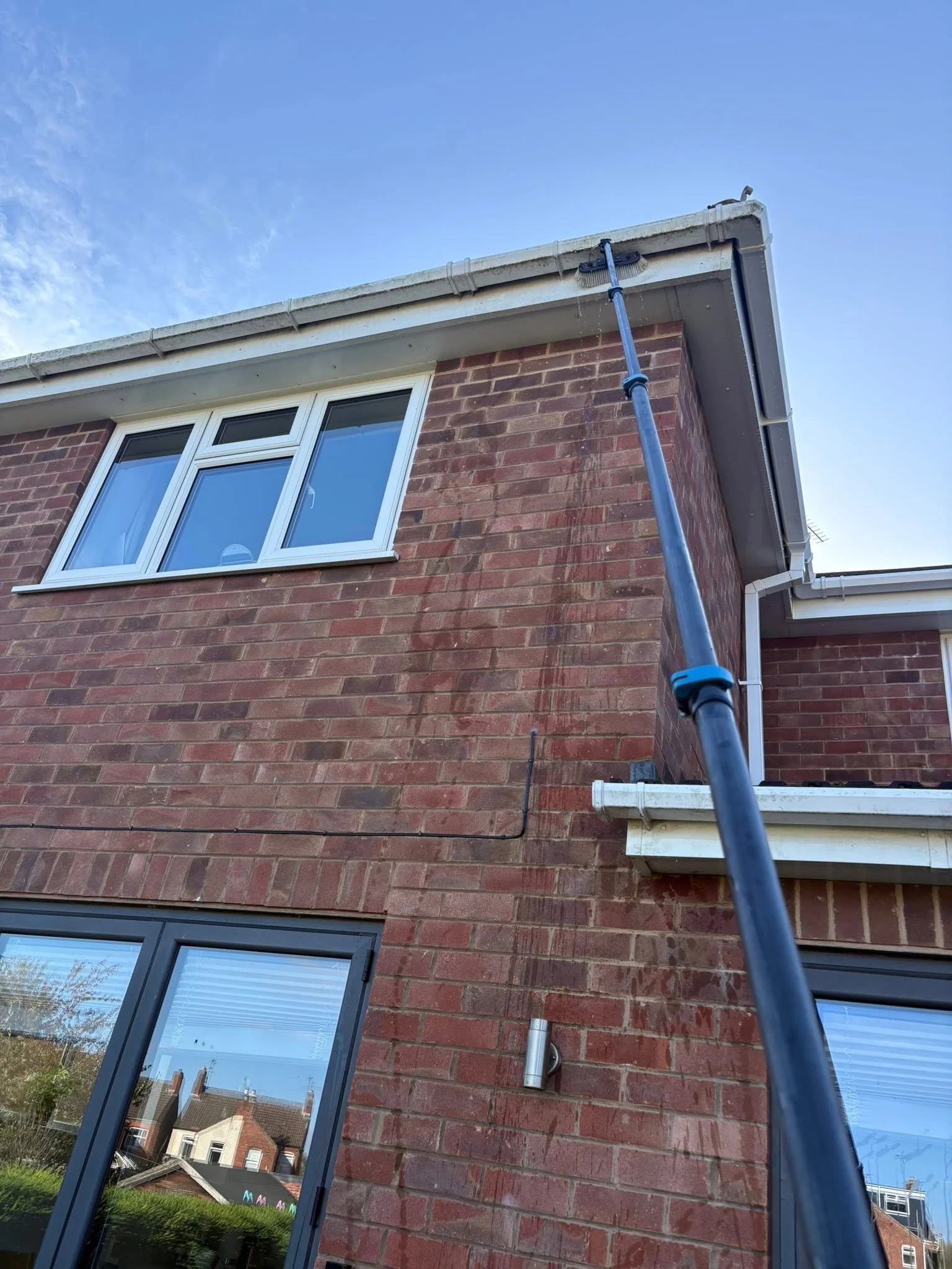 A brick house with windows and a gutter, viewed from the ground at an upward angle, with a blue sky in the background.