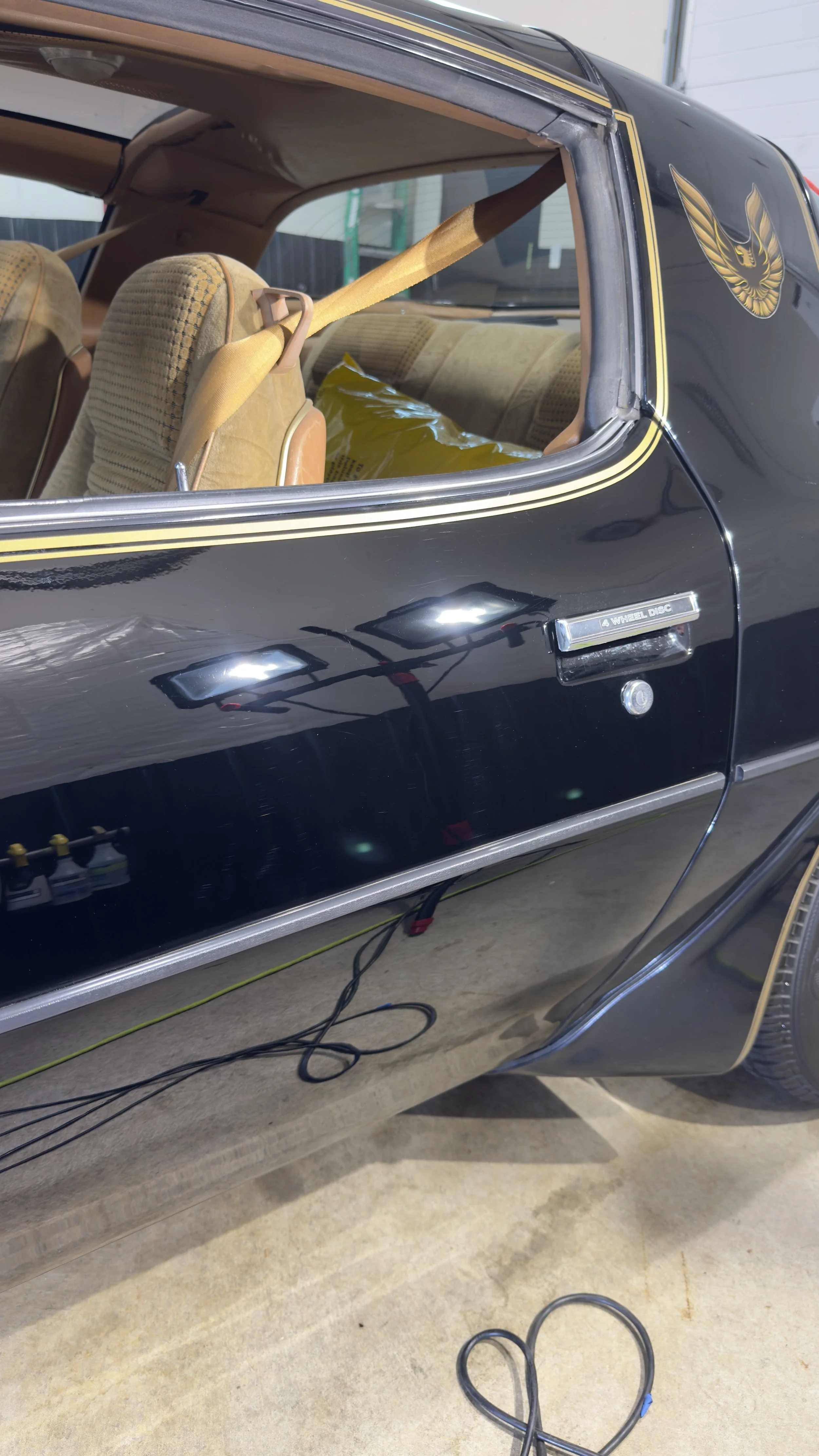 Side view of a black classic car with tan seats, parked inside a garage.