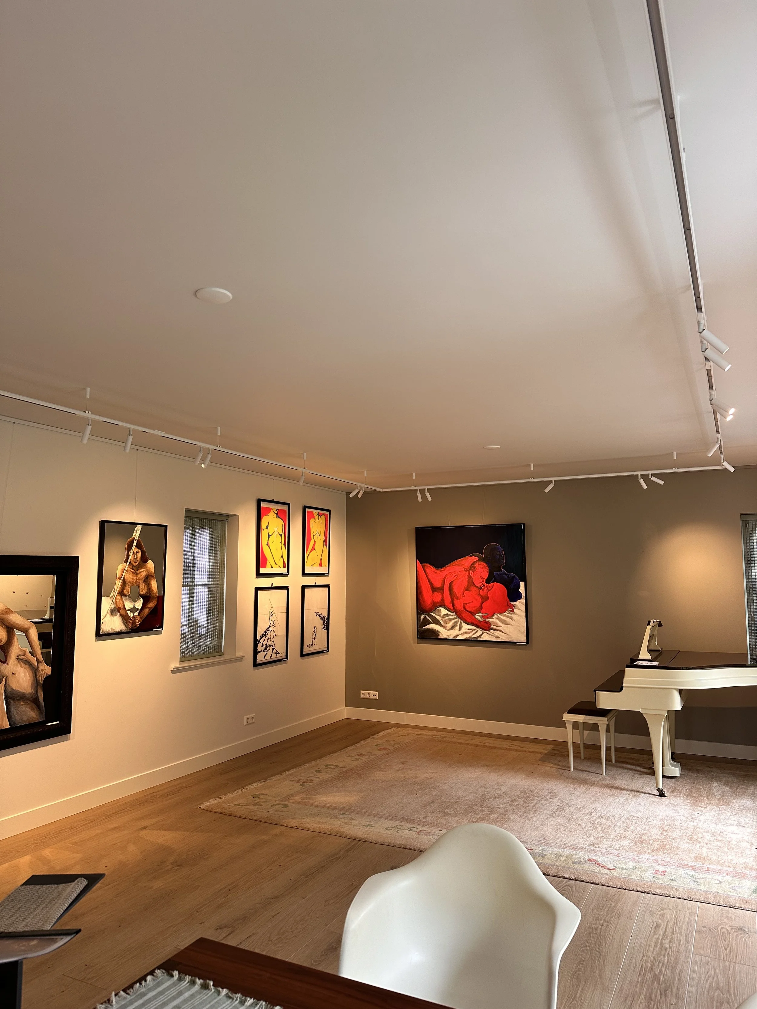 An art gallery room with various paintings on the wall, a white grand piano, and a white modern chair in the foreground.