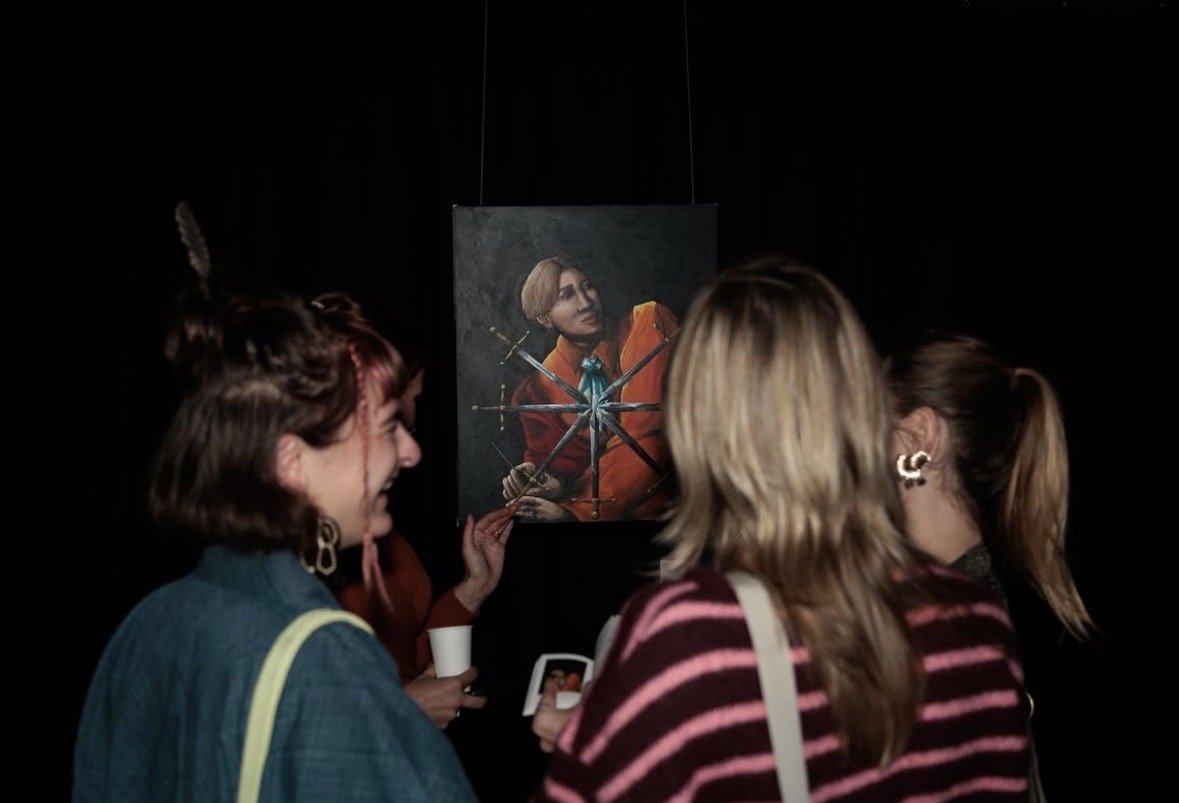 Three women looking at a portrait of a man as a modern caravaggio painting with a dark background.