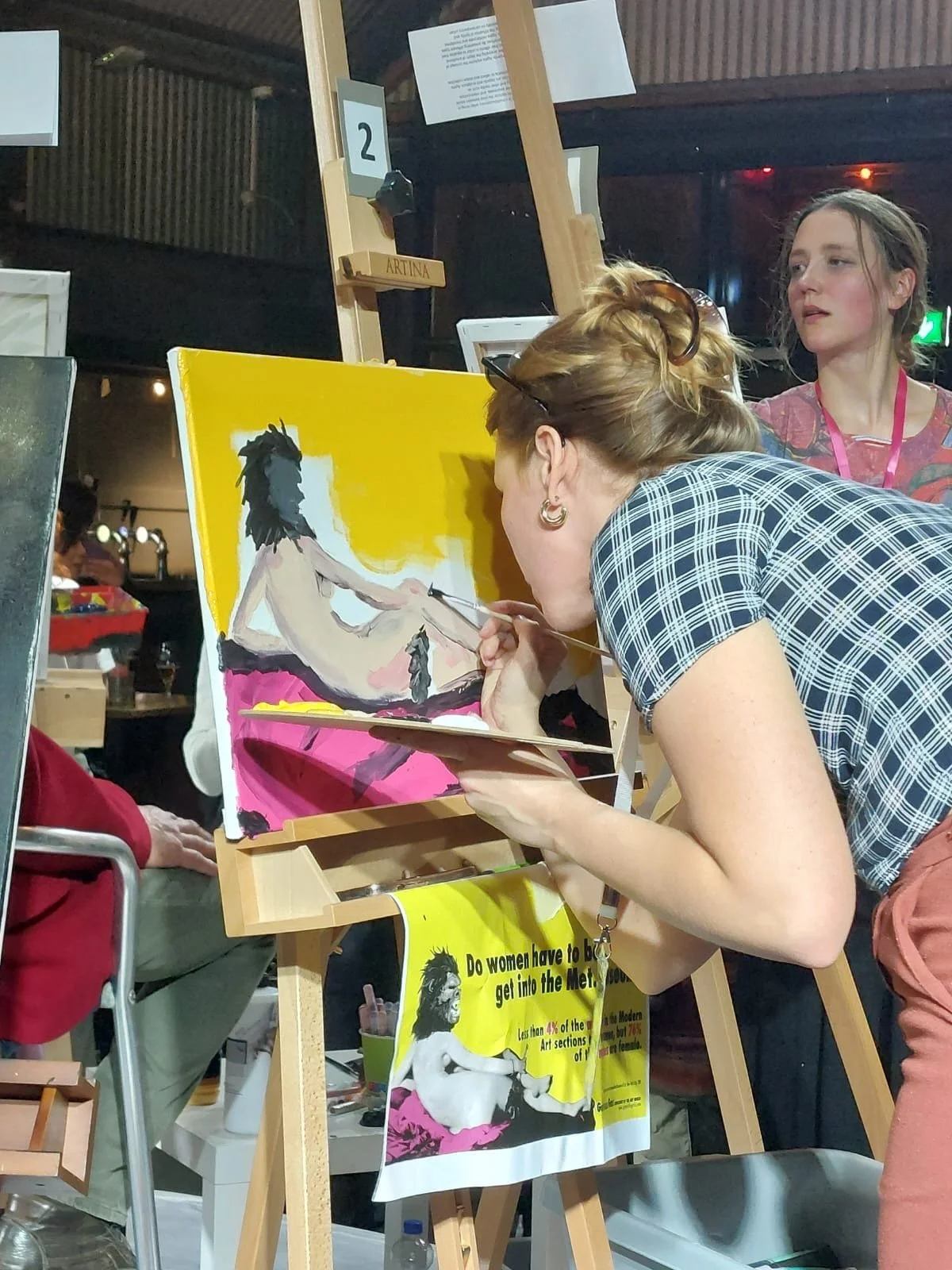 An artist painting a nude figure on a canvas at an art event or workshop.