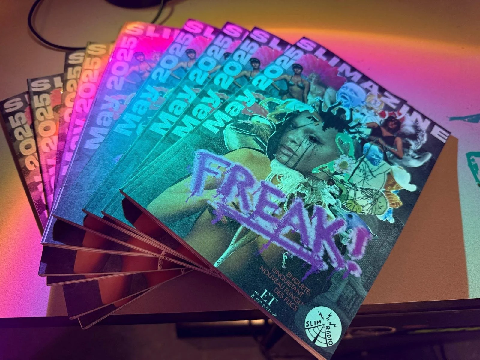 Stack of colorful magazines featuring a woman on the cover with the word "FREAK" in large purple letters, surrounded by various images and illustrations.