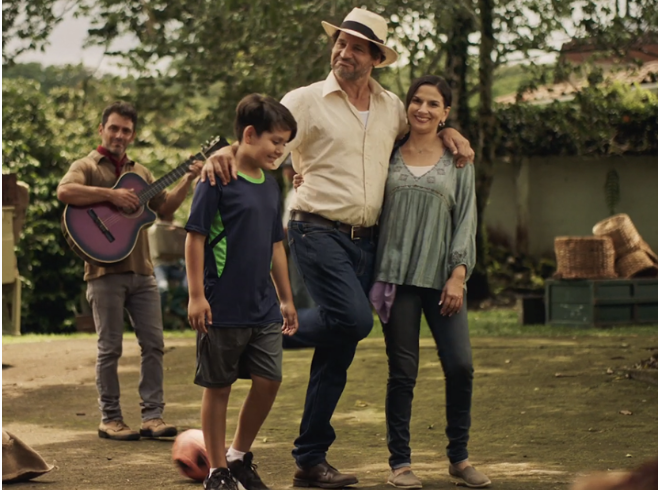 Family outdoor gathering with four members, one playing guitar, on a grassy backyard with trees and a shed in the background.