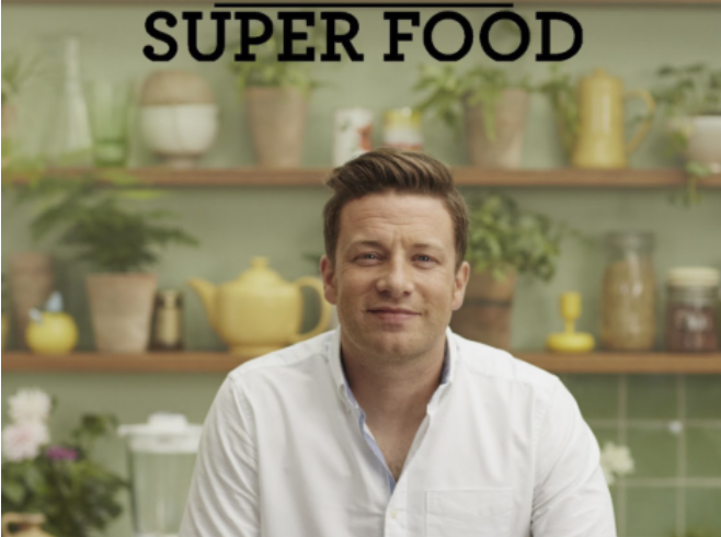 A man in a white shirt sitting in a kitchen with shelves of potted plants and kitchenware, with the words 'SUPER FOOD' in black above.