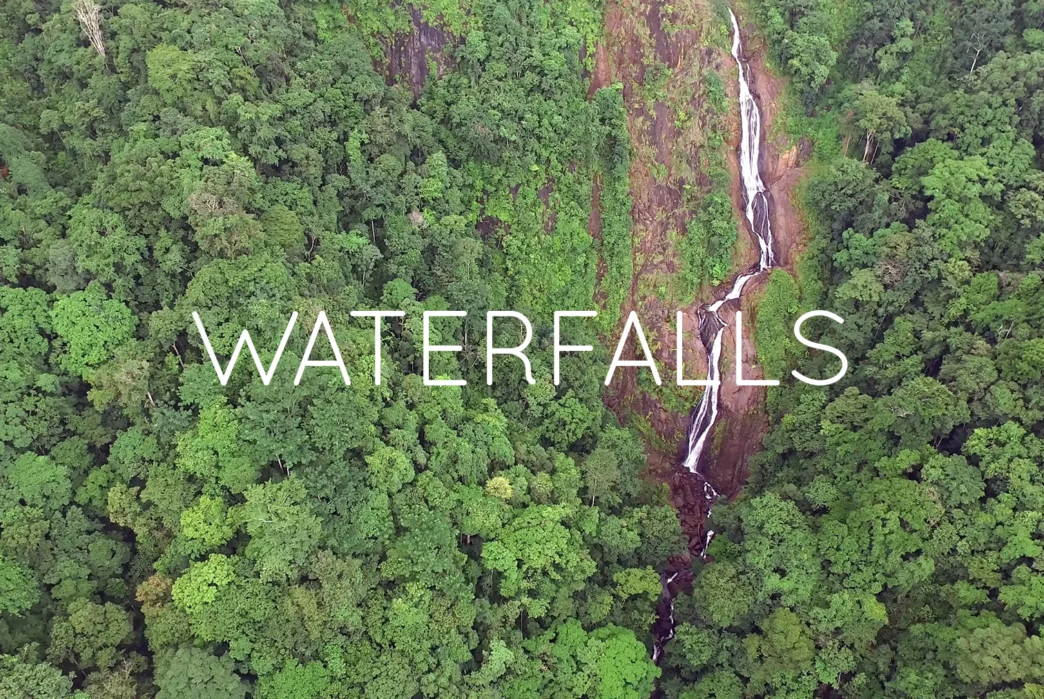 Aerial view of lush green forest with a tall, narrow waterfall cascading down a rocky cliff, accompanied by the text 'Waterfalls' overlaid on the image.
