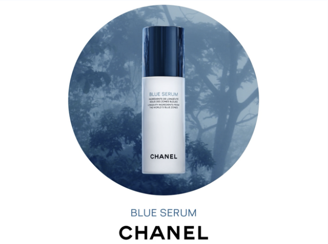 A bottle of Chanel Blue Serum skincare product with a dark blue cap, set against a blue-toned forest background.