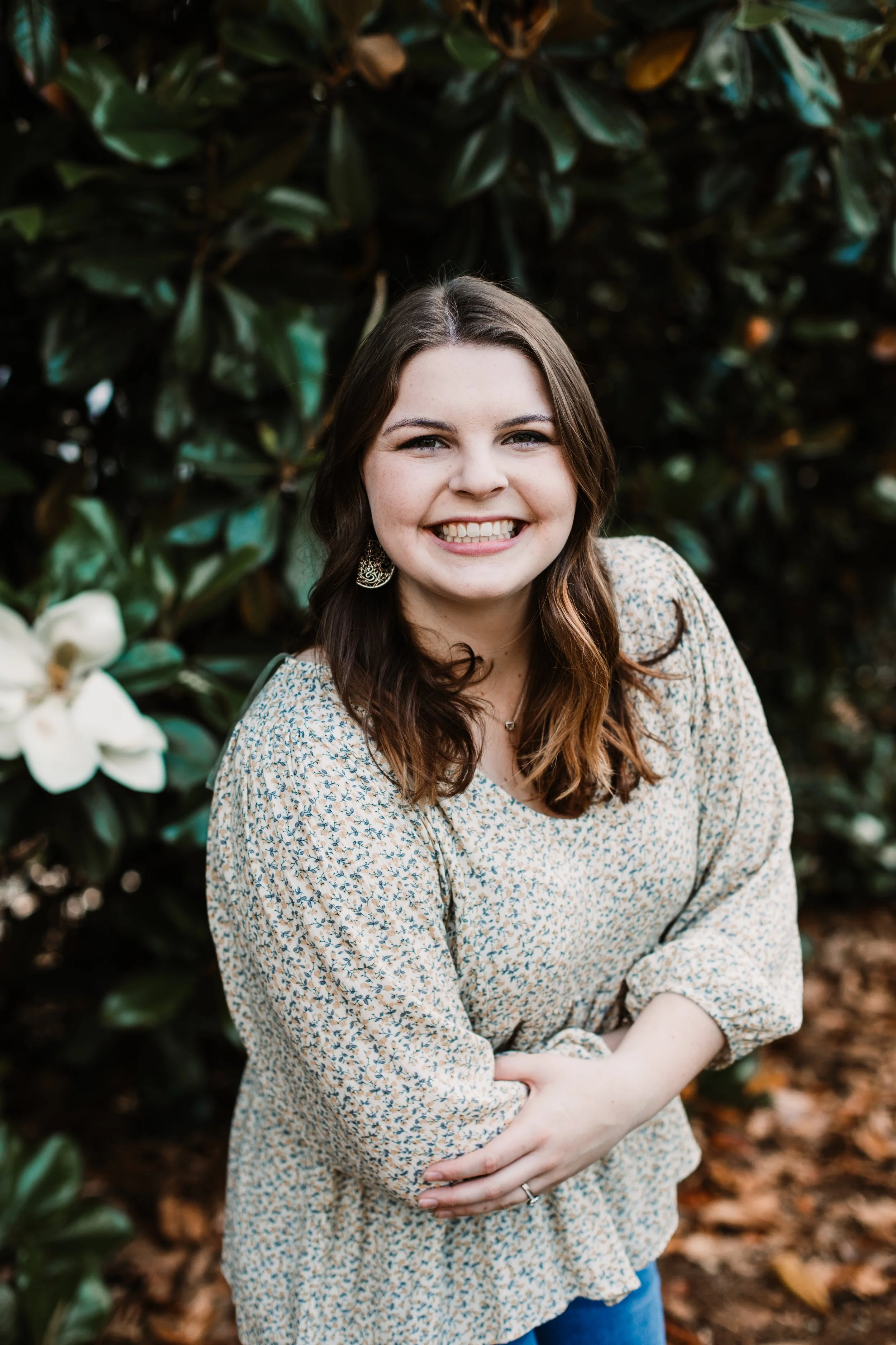 Smiling woman in a floral blouse standing among lush green plants