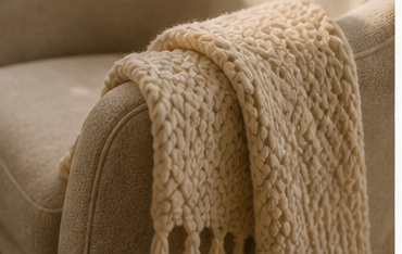 Close-up of a beige knitted blanket draped over the arm of a beige sofa.