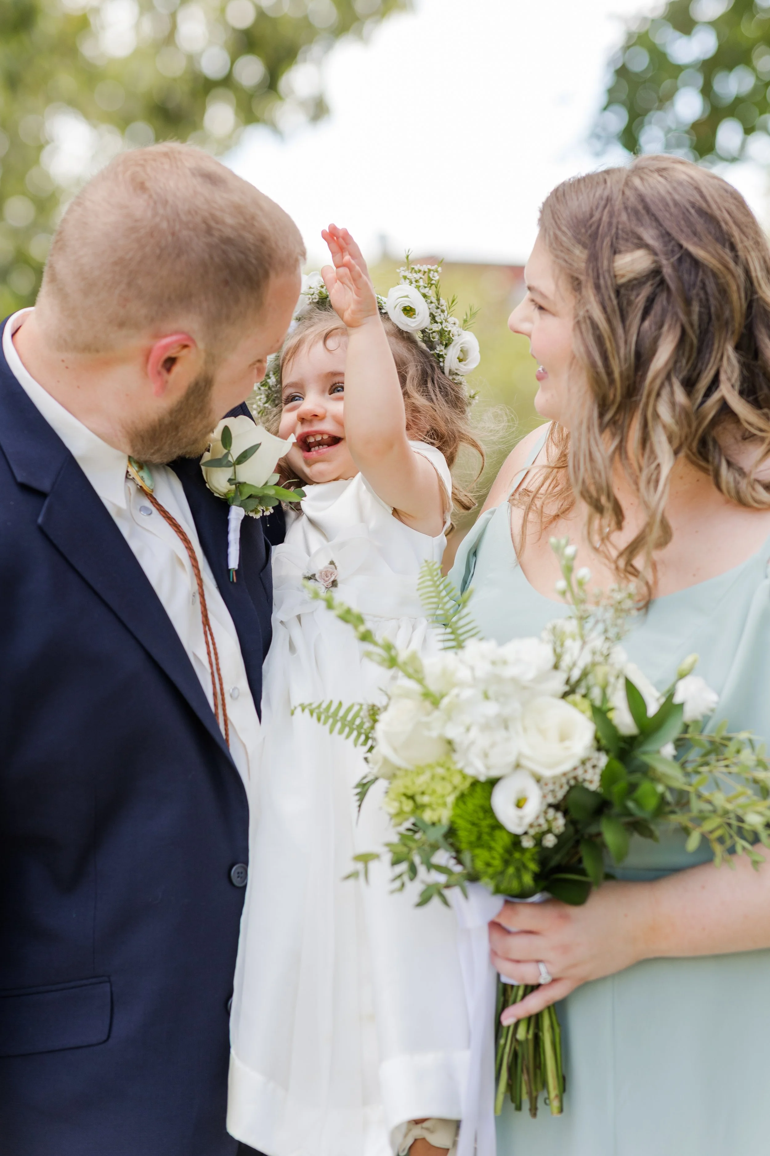 Bridesmaid, groomsman, and flower girl posing outdoors with white floral bouquets at a wedding