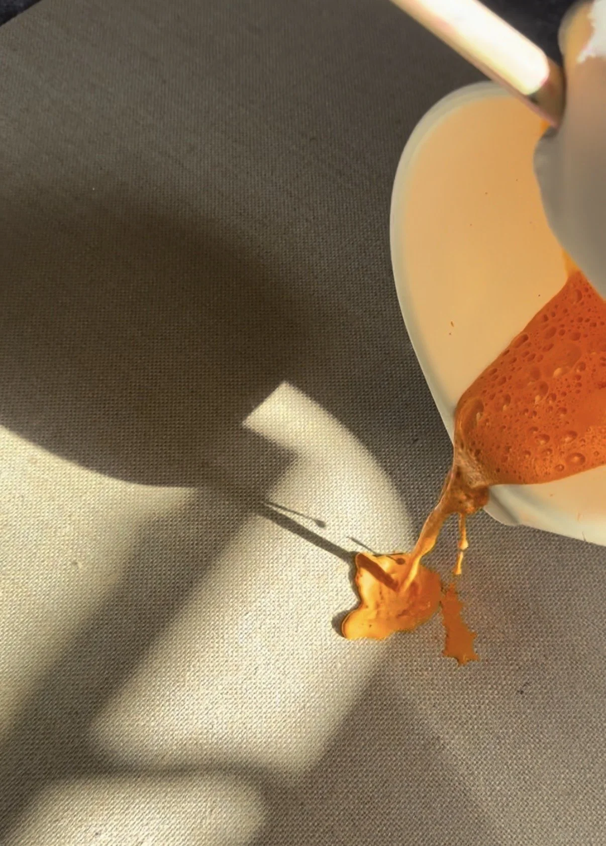 A close-up view of a coffee mug with coffee spilling out onto a gray surface.