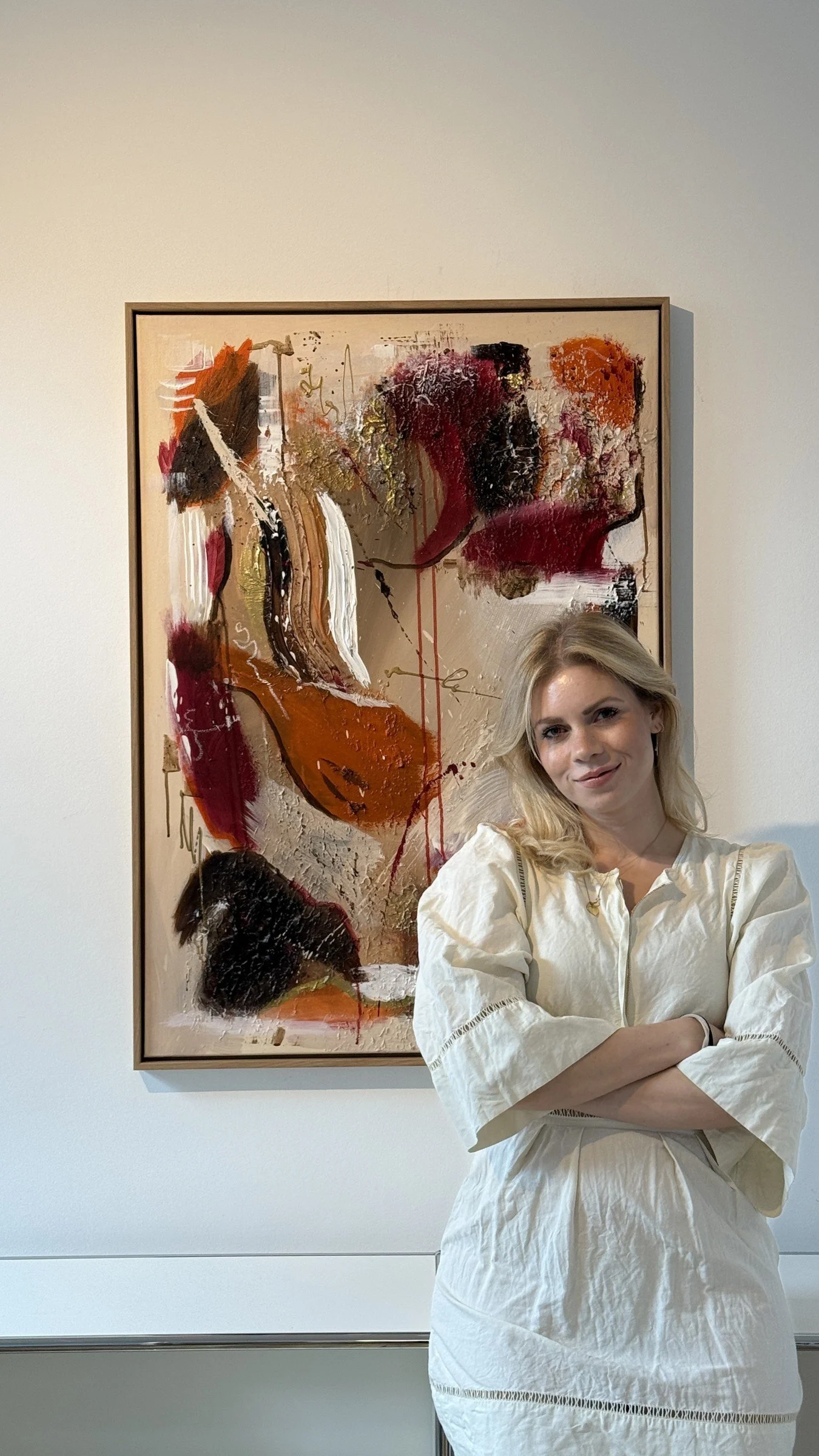 Artist Sabrina Richter standing next to one of her original abstract paintings in red, orange and gold