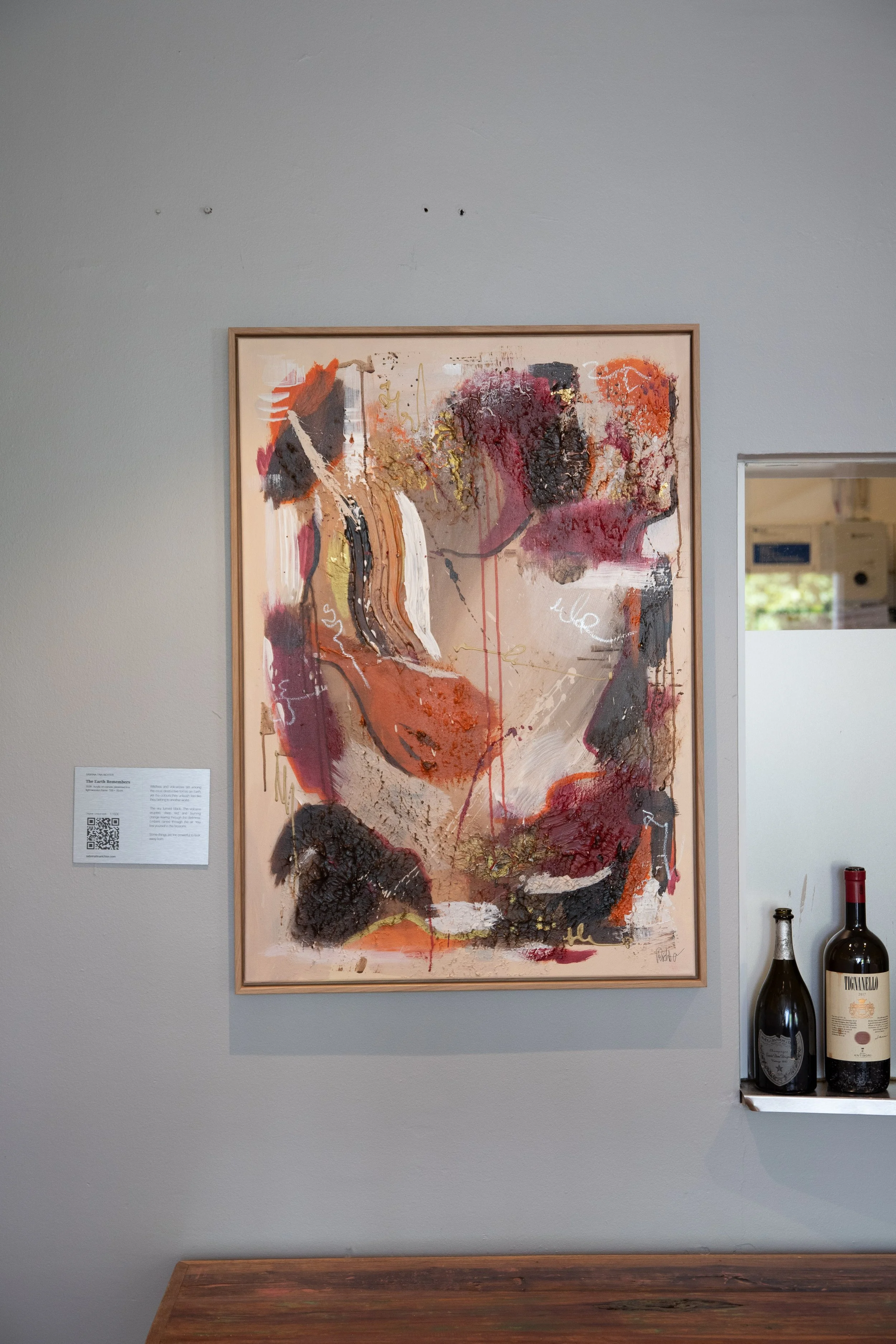 Abstract painting with warm colors, textural elements, and scribbled writings hanging on a light gray wall.