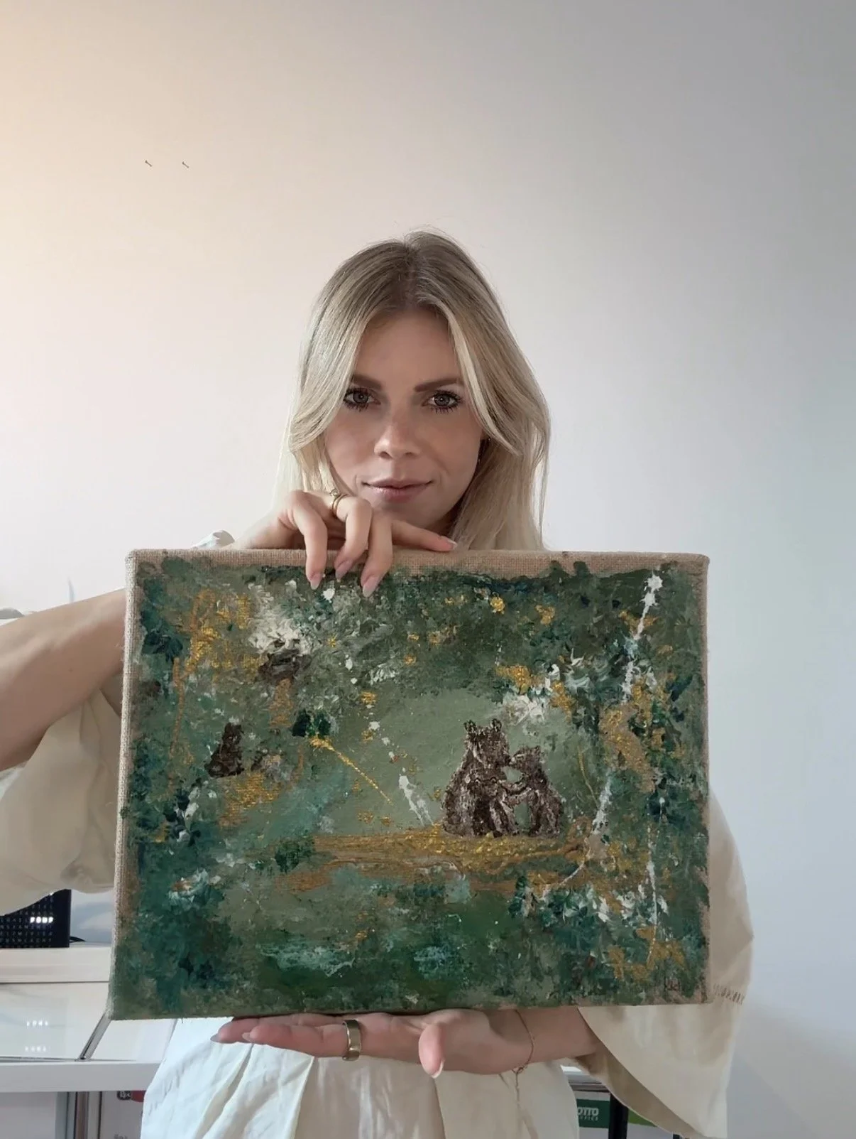 Woman holding a painting that depicts animals in a lush green landscape.