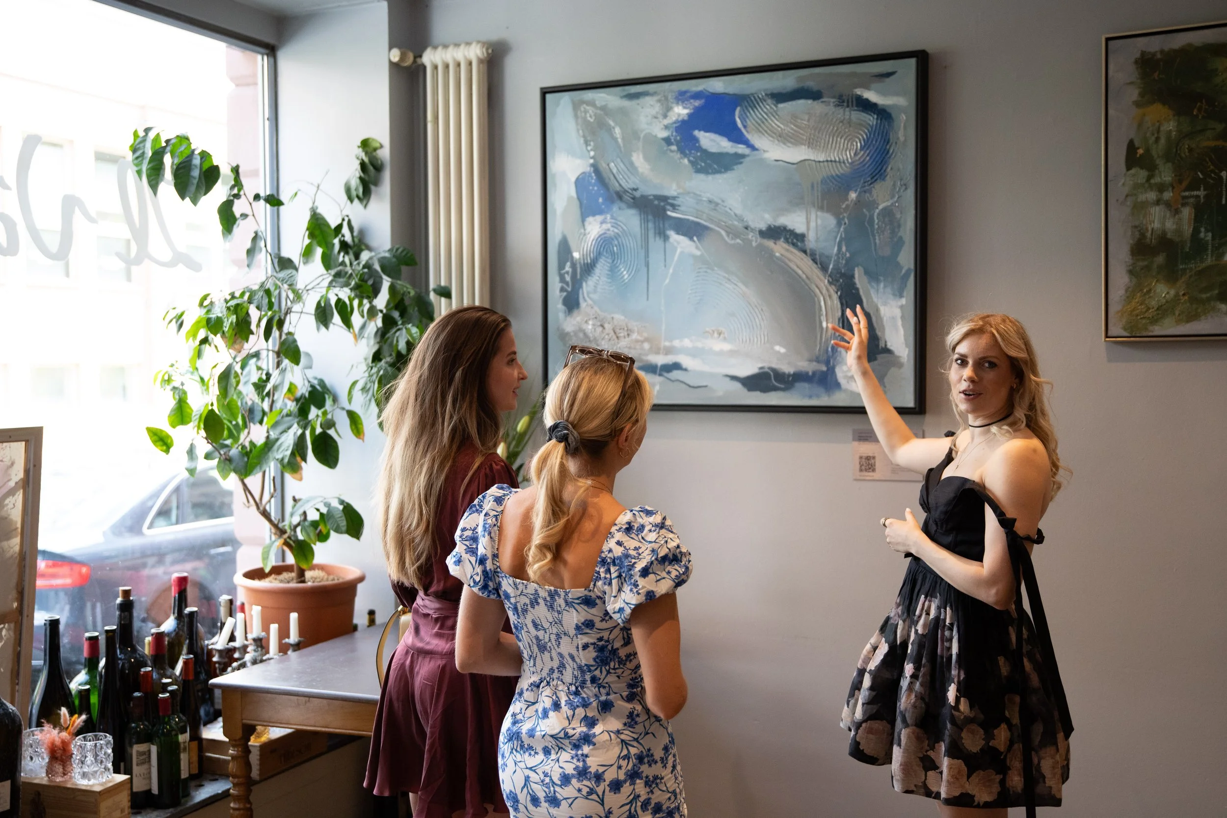 A group of four women enjoying a conversation in an art gallery, with two modern abstract paintings hanging on the wall behind them.
