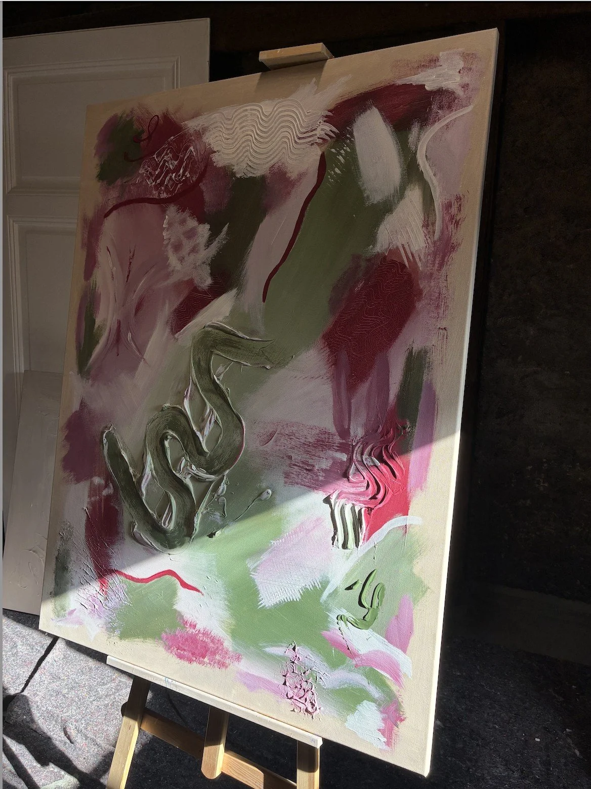 Original abstract acrylic painting in green and pink with thick texture on an easel in the studio of Sabrina Richter