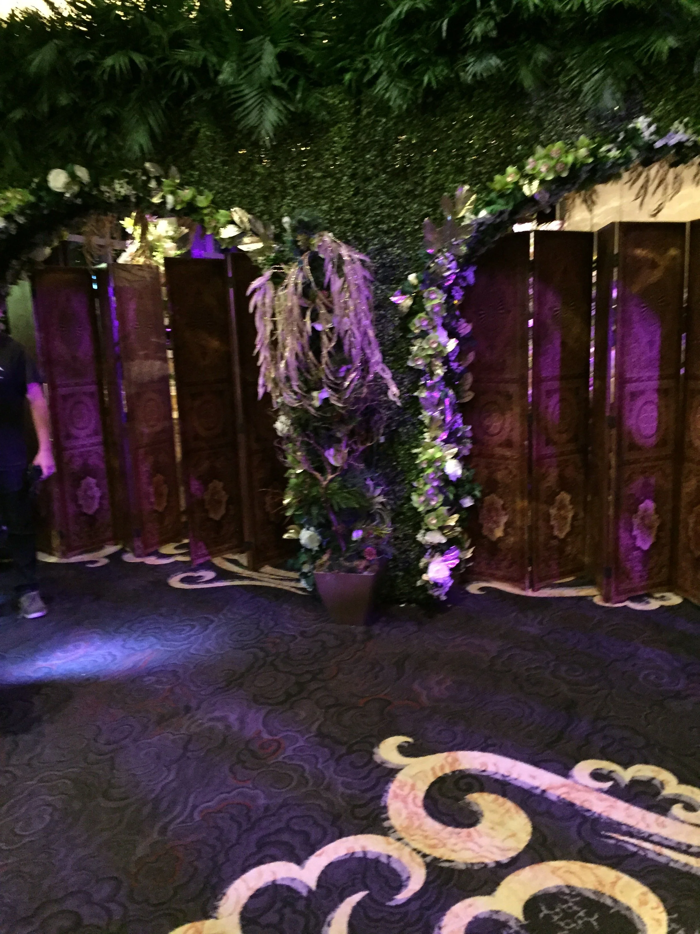 A floral arrangement in front of a wooden screen on a patterned carpeted floor, with purple lighting.