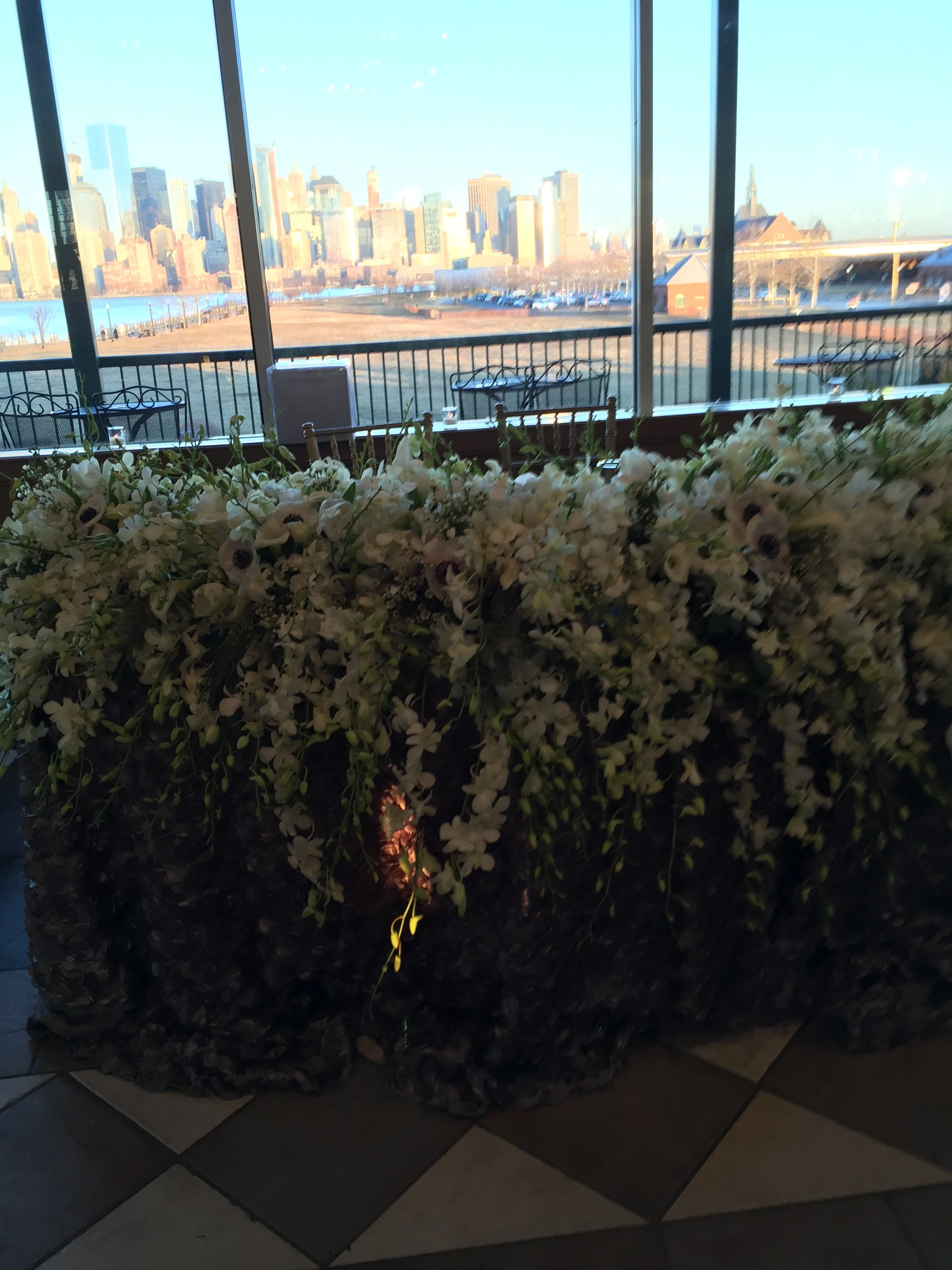 Indoor flower arrangement with white flowers in front of large windows overlooking a city skyline
