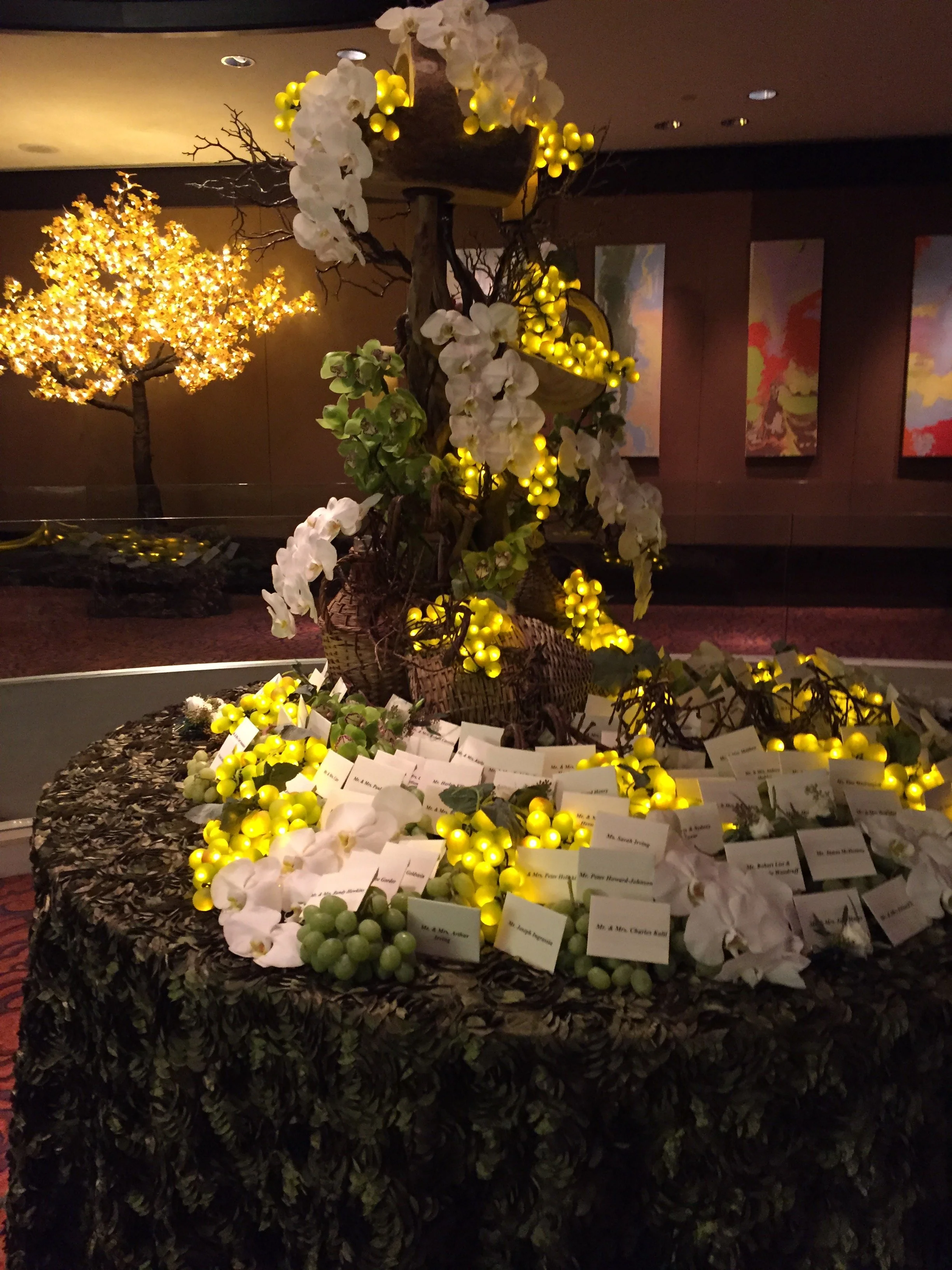 Display of illuminated decorative flowers and name cards on a black, leafy-textured table at an indoor event.