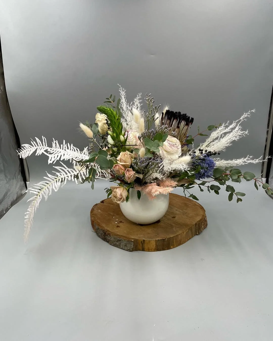 A floral arrangement in a white vase placed on a wooden cut tree slab.