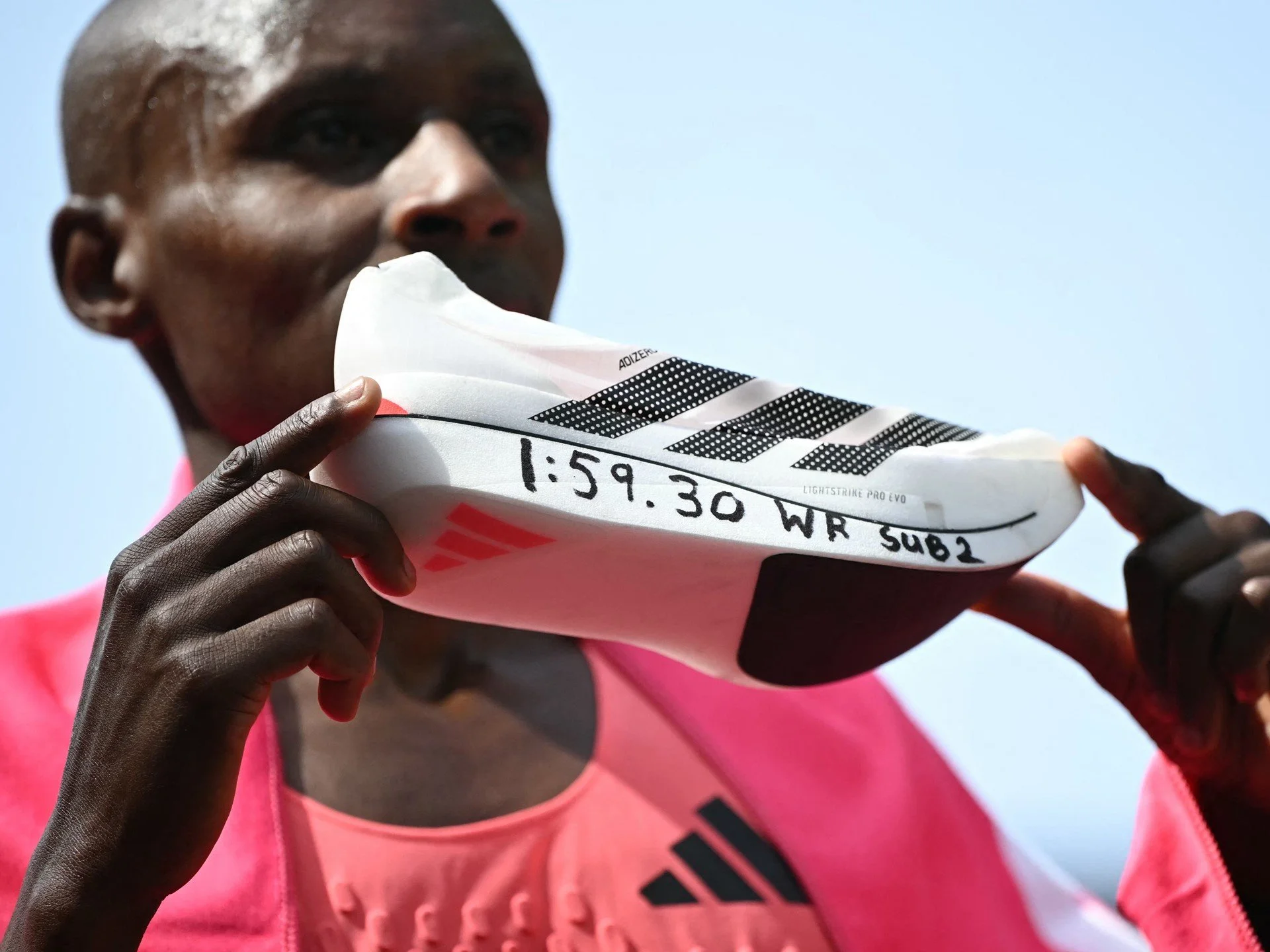 Athlete in pink workout clothes holding a white athletic shoe with black stripes and handwritten details.