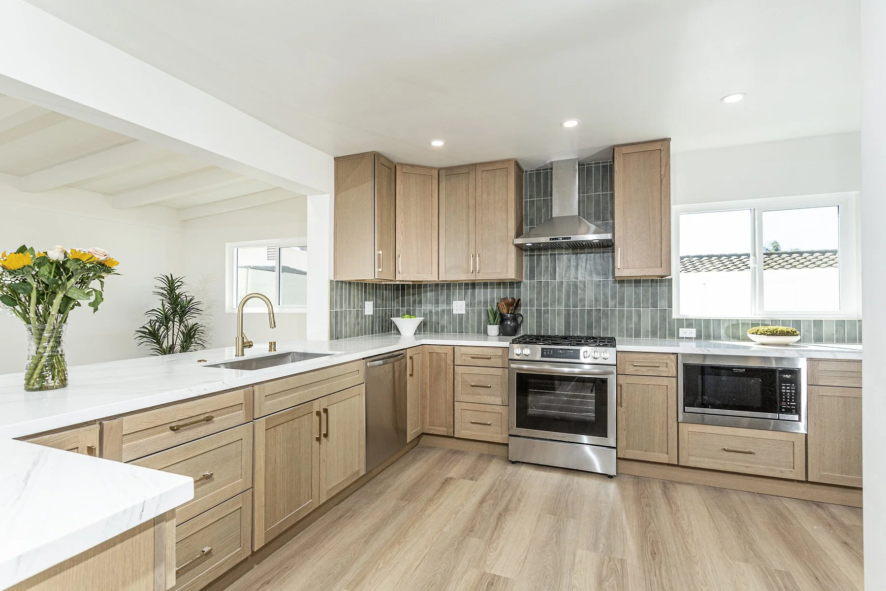 Modern kitchen with light wood cabinets, white marble countertops, stainless steel appliances, green tile backsplash, and two windows bringing in natural light.