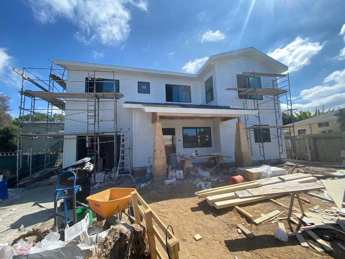 Under construction house with scaffolding on the balcony, tools, and building materials scattered around the yard.