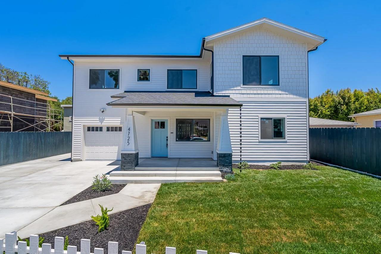 Modern two-story white house with a front porch, small front yard, and driveway, under a clear blue sky.