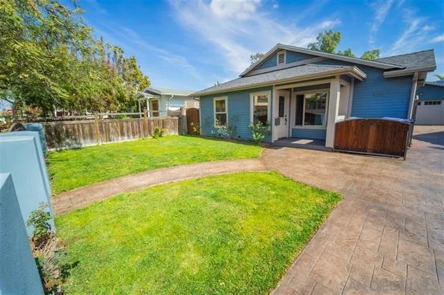 Front yard of a blue house with a curved walkway, green grass, a wooden fence, and a driveway leading to a two-car garage.