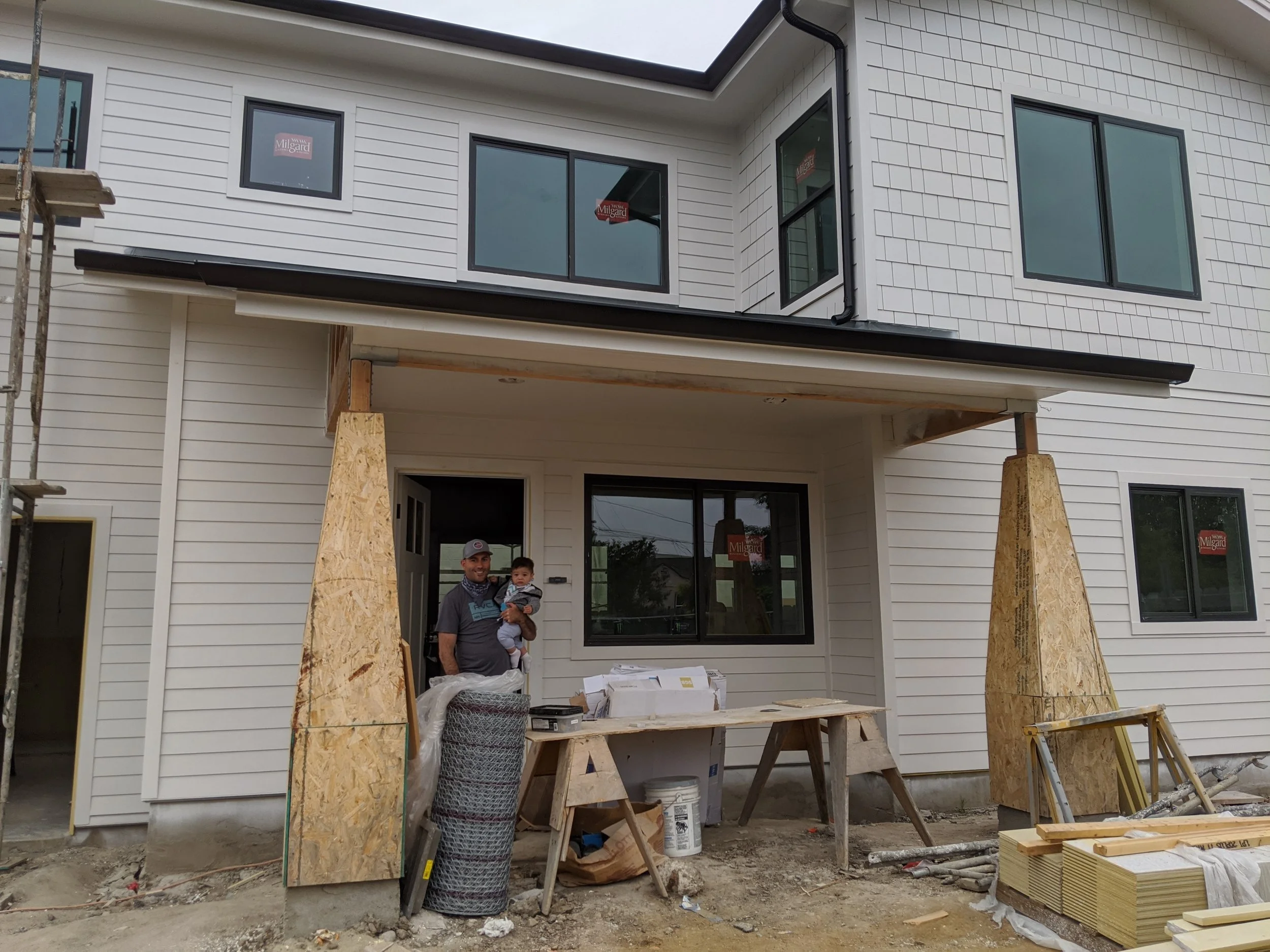 A man and a child standing outside a house under construction, with building materials and scaffolding around.