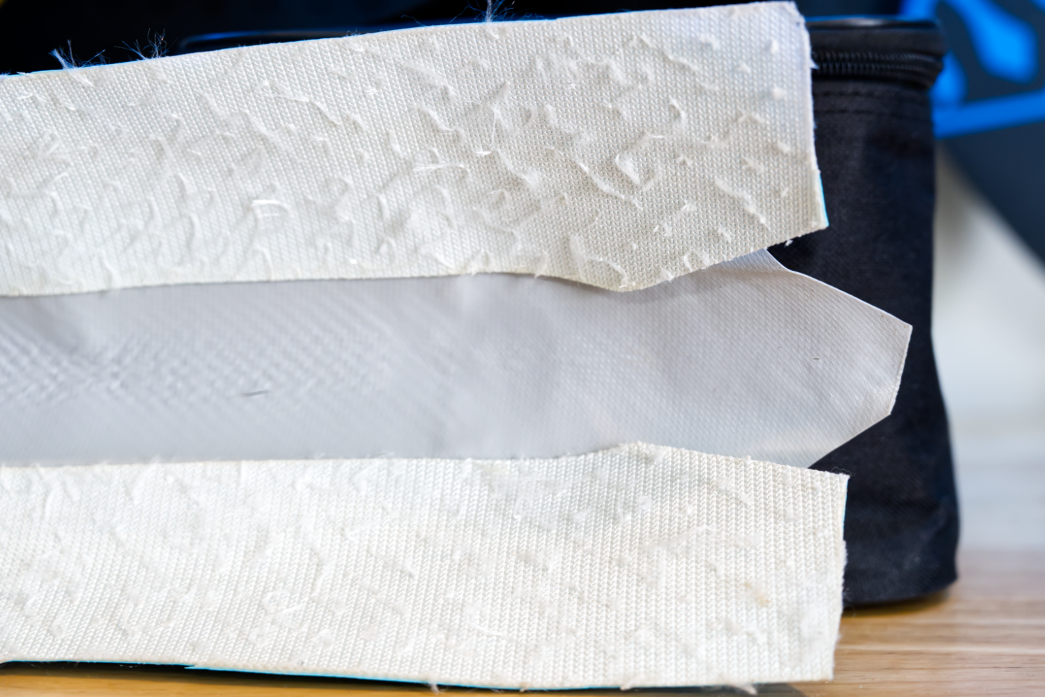 A section of an iSUP rail that has been cut out to show the top and bottom layers joined with a third layer of PVC tarpaulin to form the rail edge.