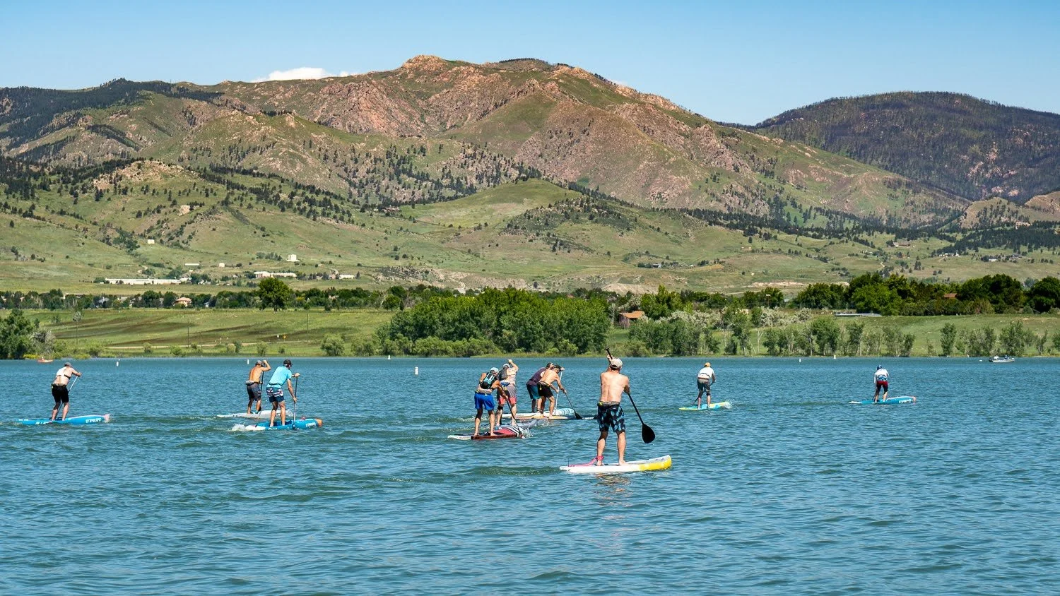 paddle board racers on a lake in front of a mountain