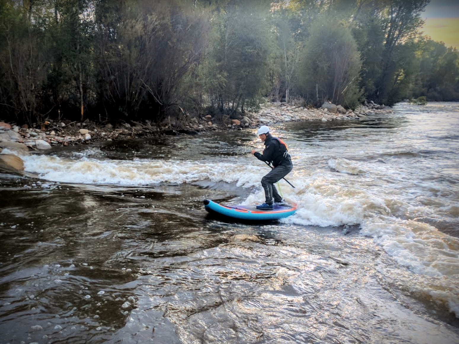 whitewater paddleboarder surfing a river wave