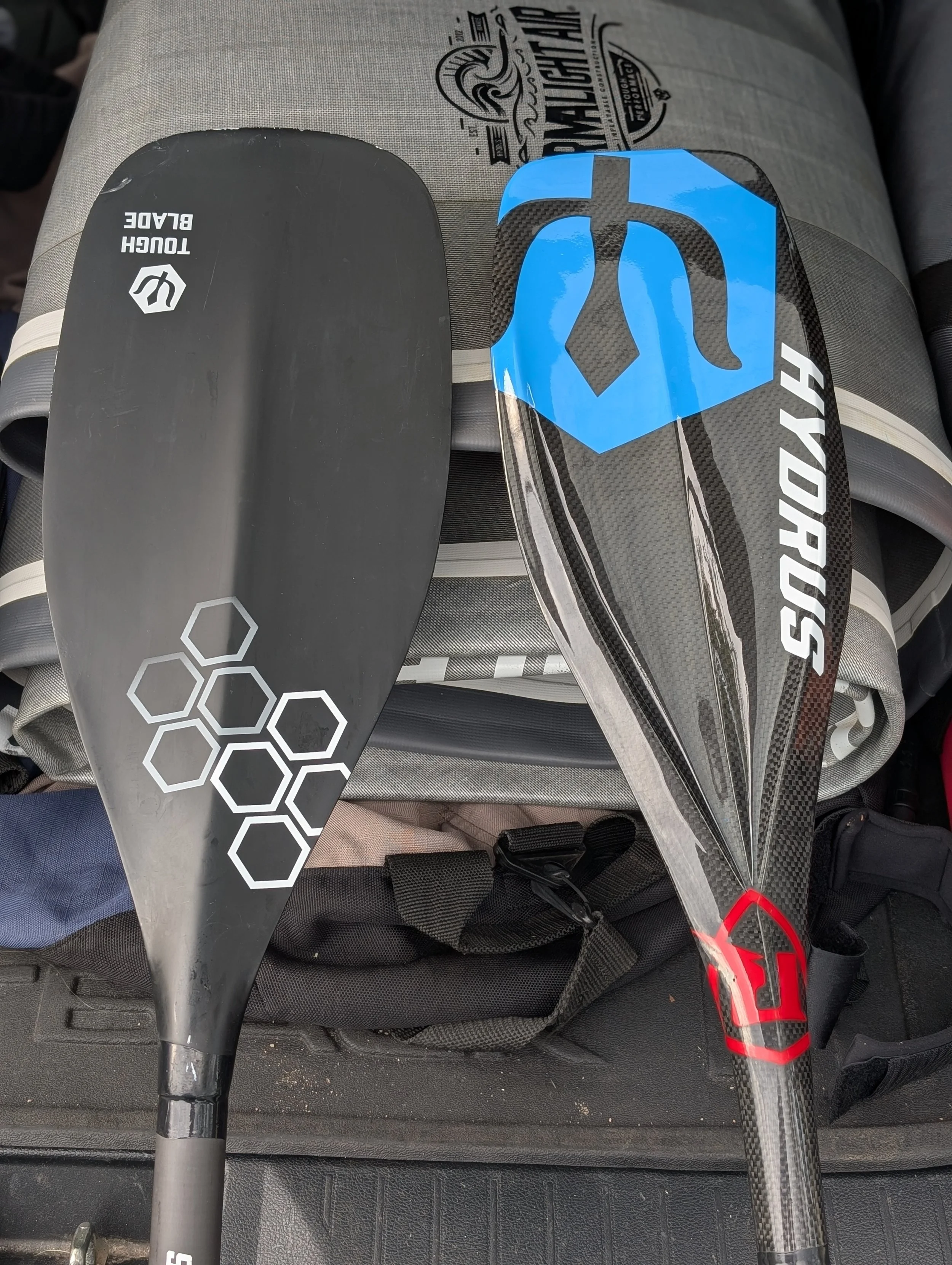 The Hydrus Tough Blade paddle and Ruckus paddle next to each other sitting against a rolled up Hydrus iSUP.