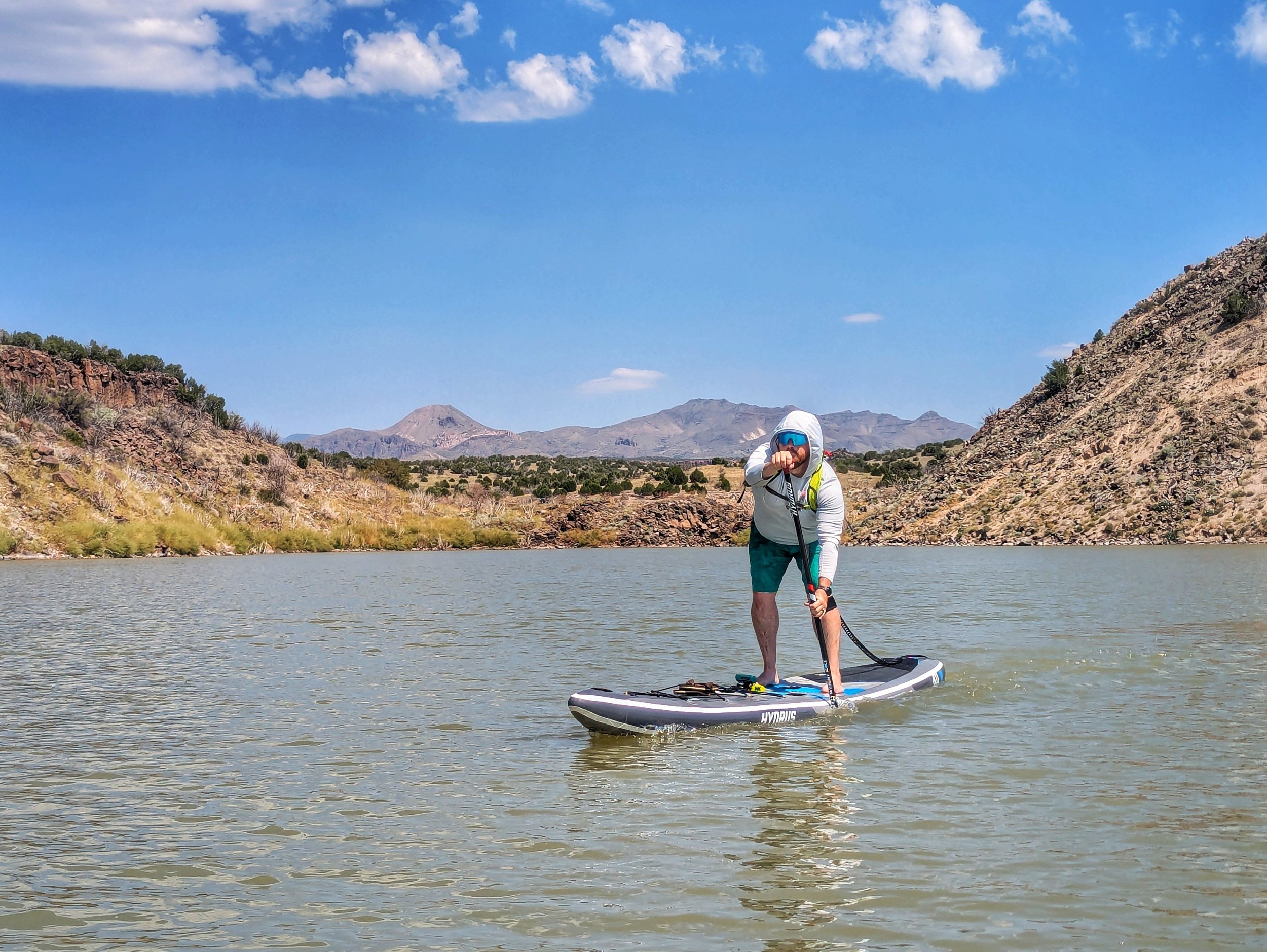 Paddling the Hydrus Elysium Air across a desert lake with mountains in the background.