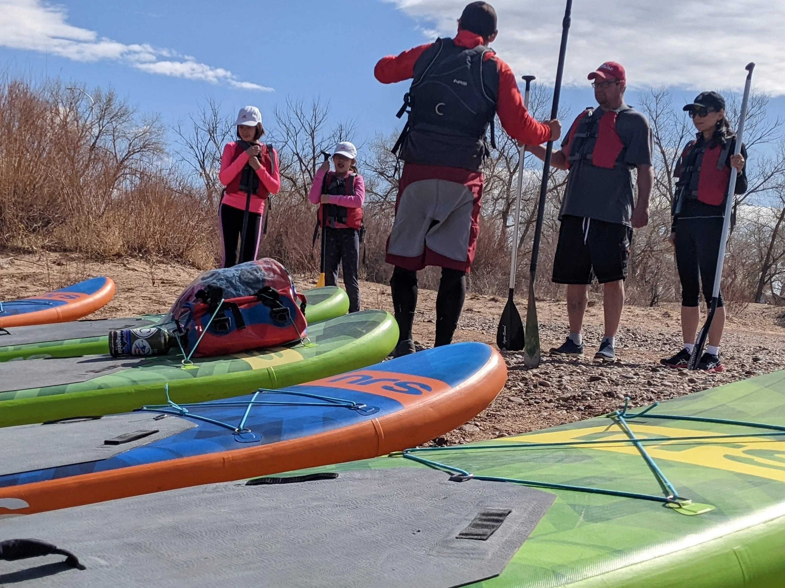 an instructor talks to a group of paddlers standing in front of their boards