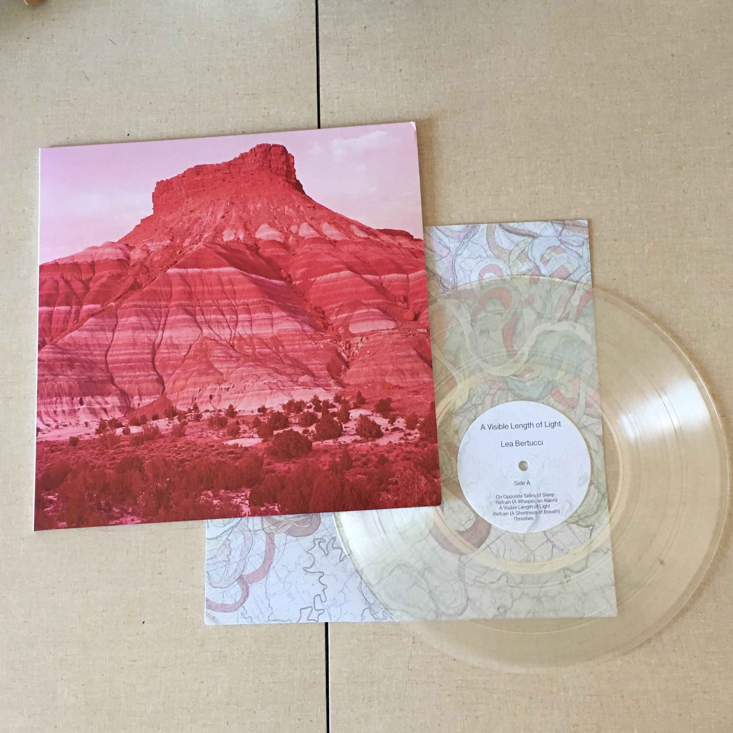 A poster of red mountain with desert landscape at base, pink sky background, and a small white paper with text attached to the bottom right corner of the poster.