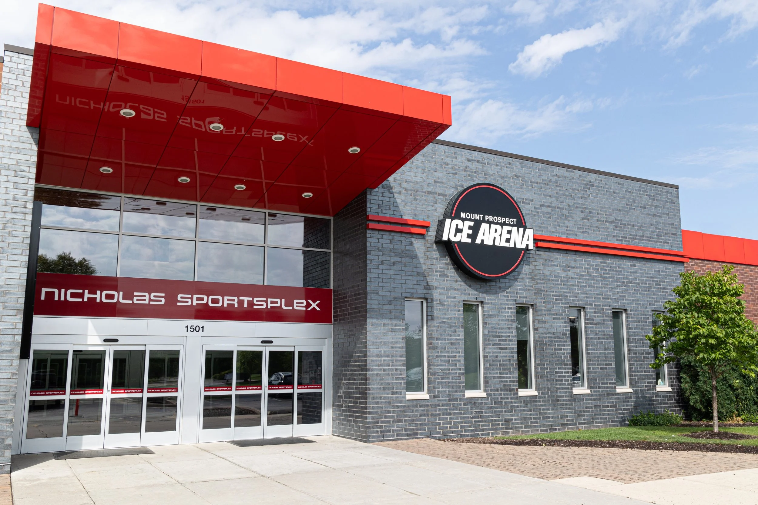 Exterior view of the Mount Prospect Ice Arena and Nicholas Sportsplex building with a modern gray brick facade, red accents, and the facility's signage.