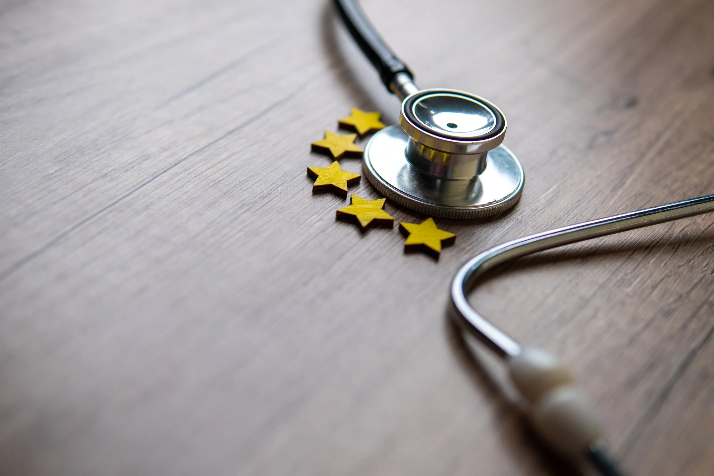 A stethoscope lying on a wooden surface next to small yellow star-shaped objects.