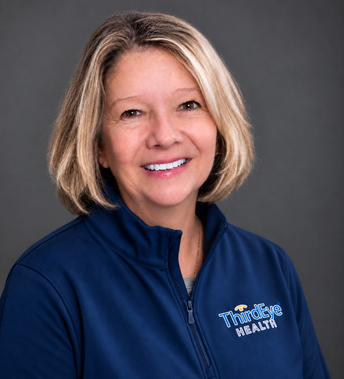 A middle-aged woman with blonde hair, smiling, wearing a navy blue sports jacket with a "ThirdEye Health" logo, posed against a gray background.