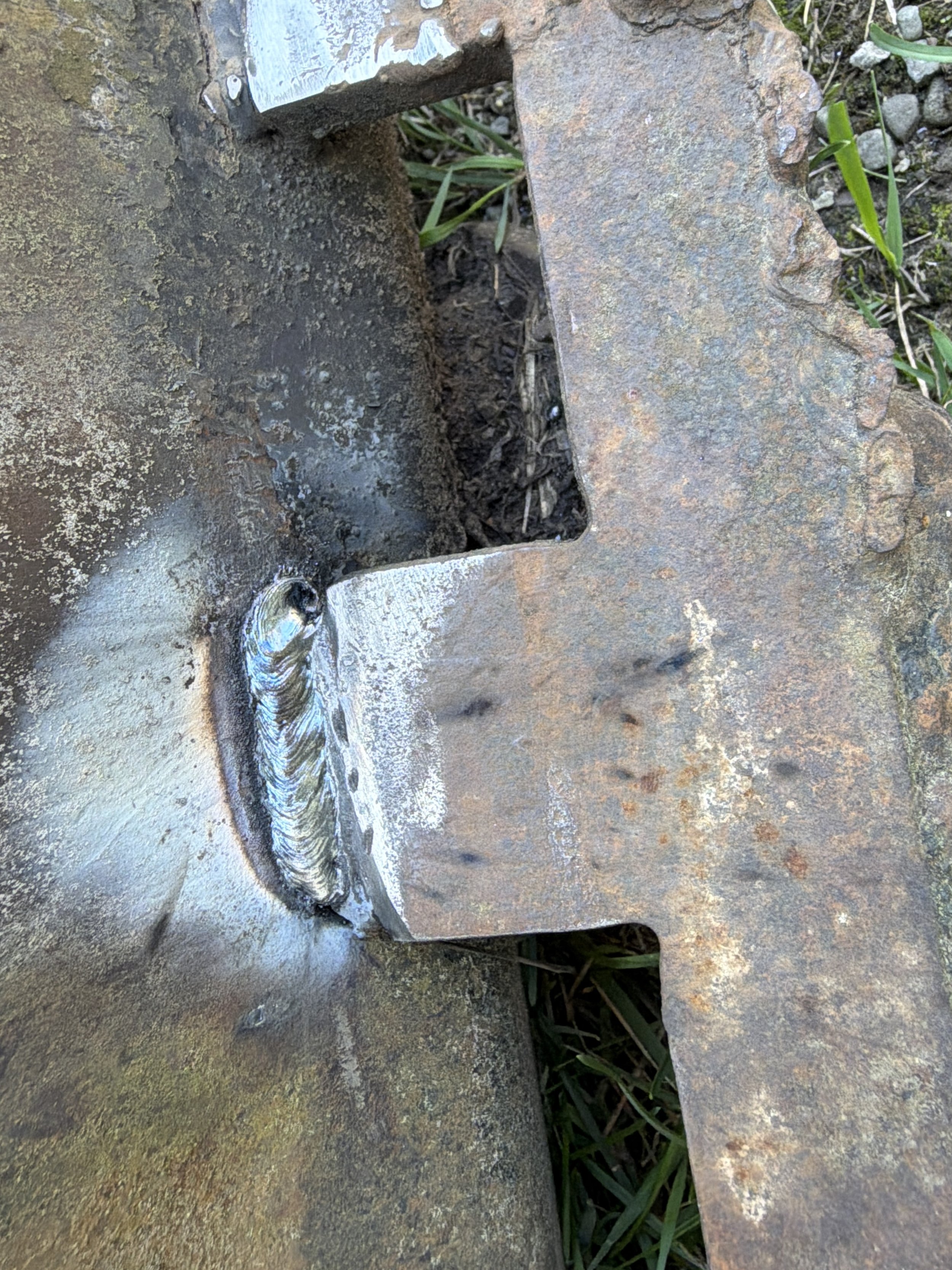Close-up of a rusted metal surface with a small opening, revealing dirt and grass underneath.