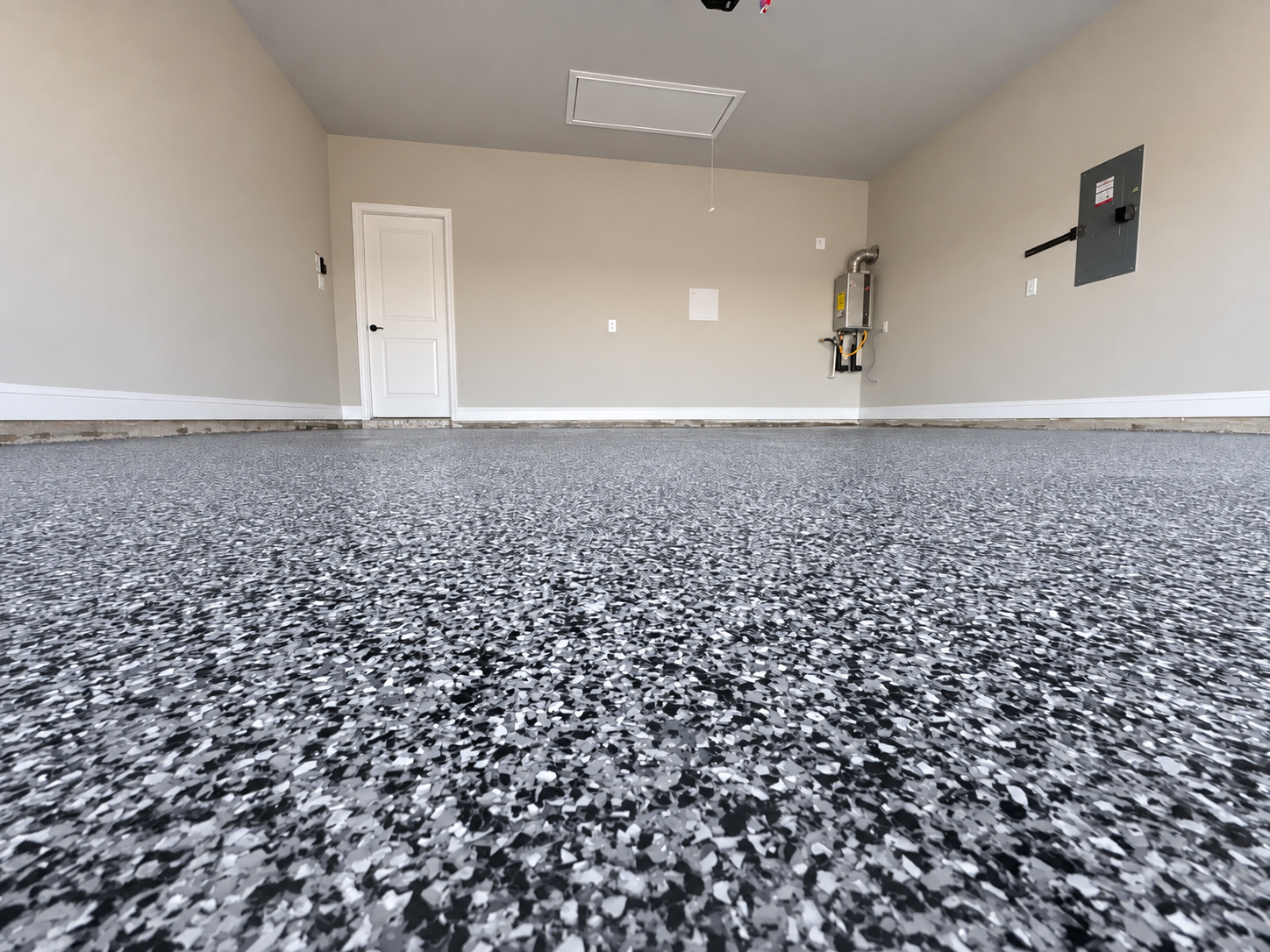 Empty garage with a speckled black, white, and gray epoxy floor, a closed white door, and various utility panels on the walls.