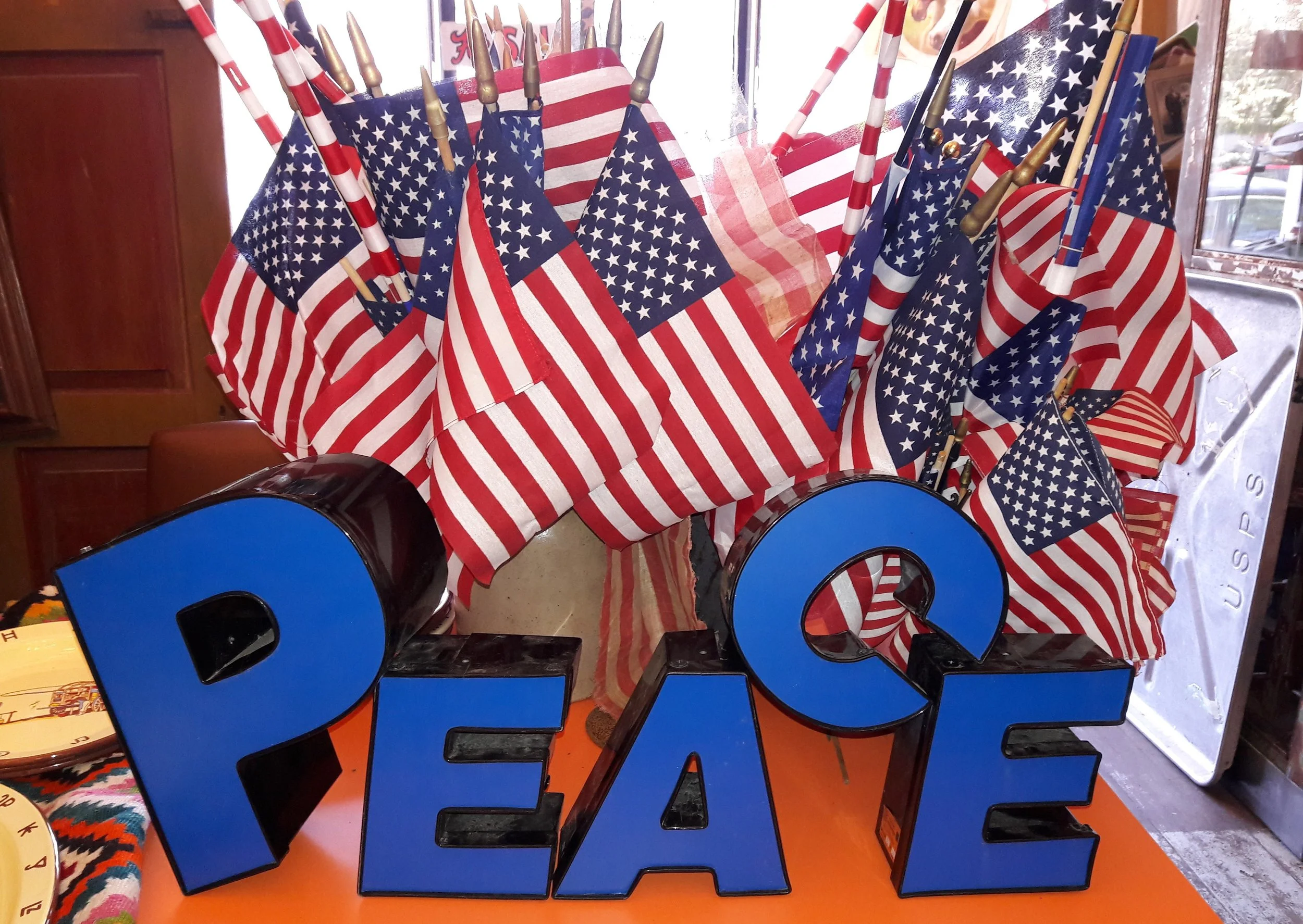 Decorative display with multiple American flags and large blue letter number '2024' on an orange table inside a store or restaurant.