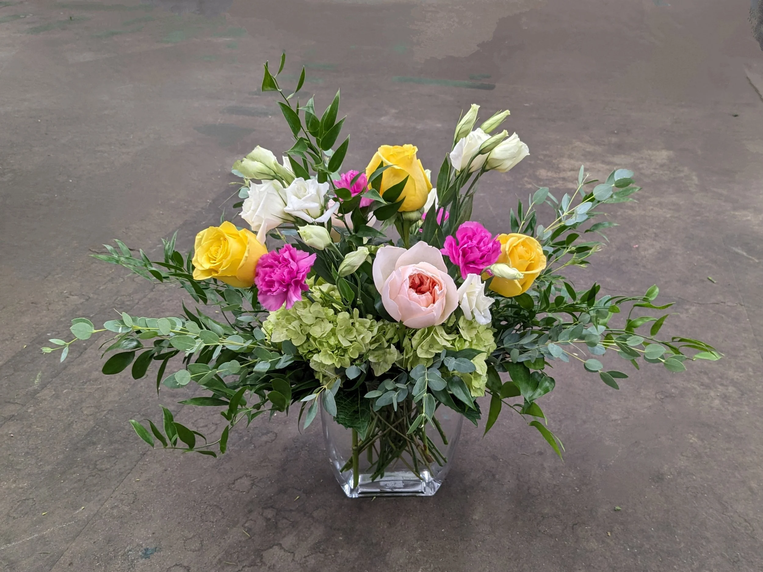 A bouquet of colorful flowers in a clear glass vase on a concrete surface.