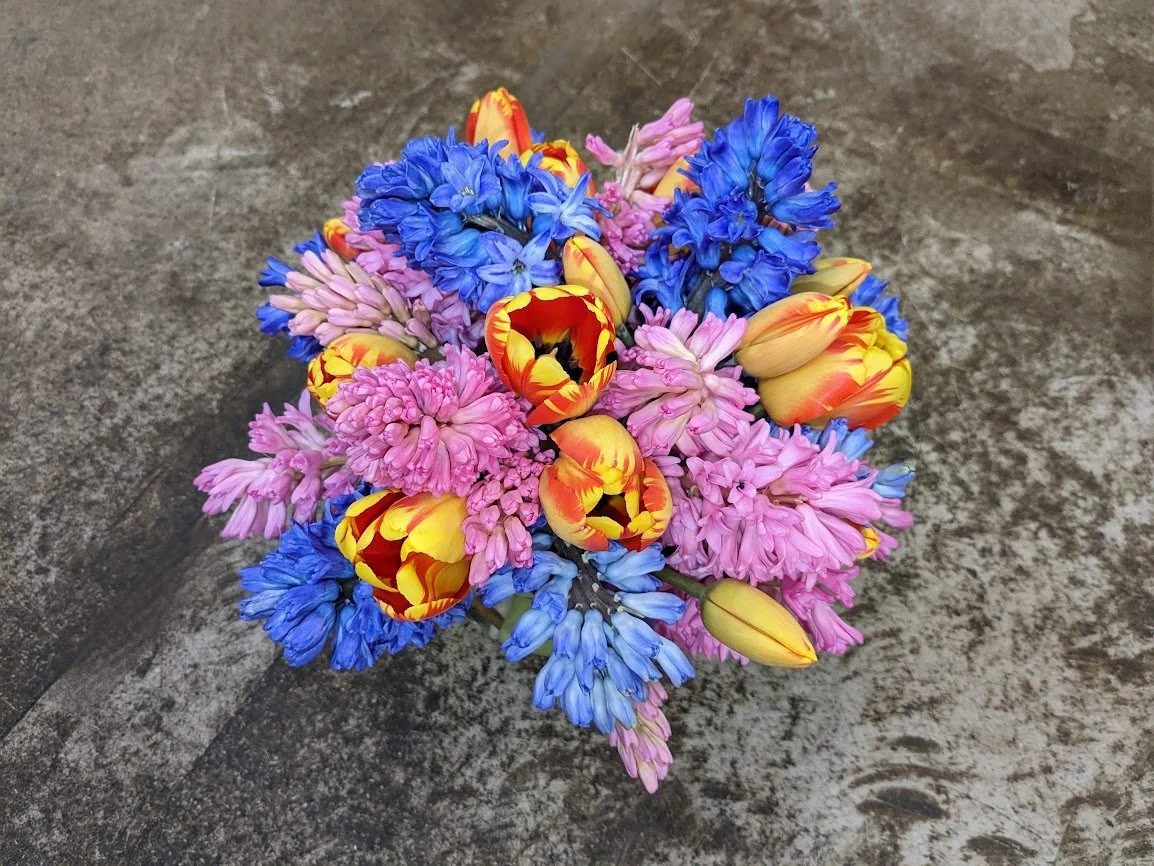 Colorful bouquet of pink, yellow, orange, and blue flowers on a wooden surface.