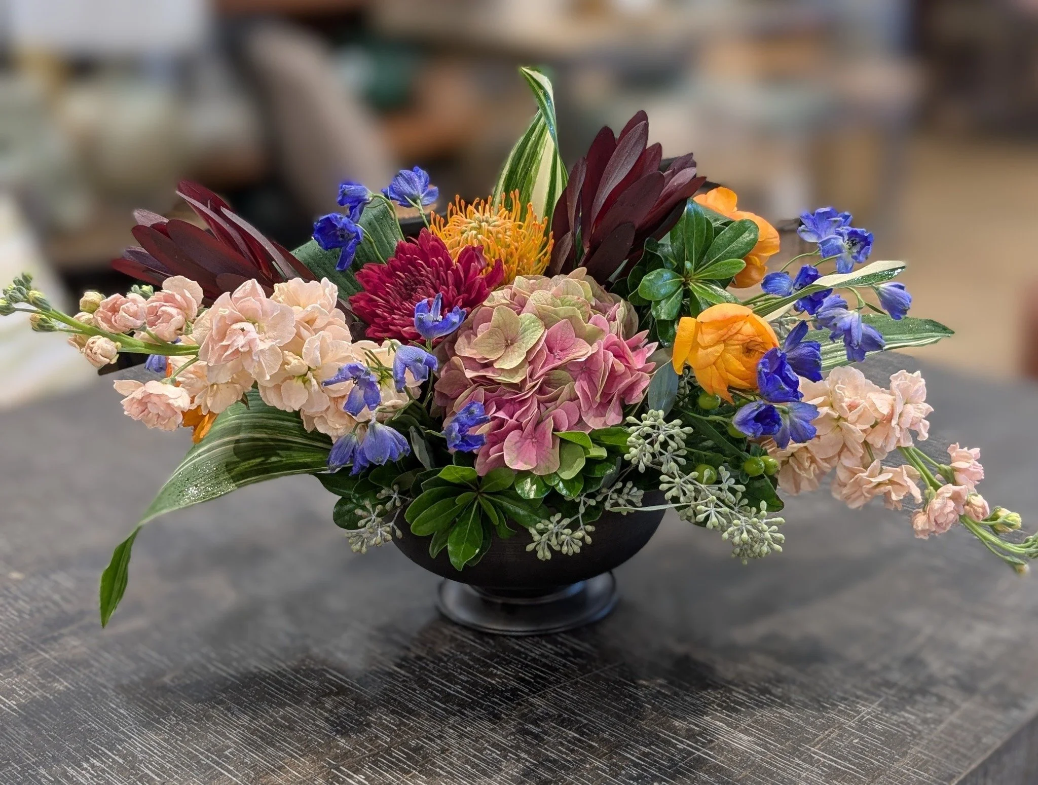 A colorful flower bouquet in a black vase placed on a dark textured surface.
