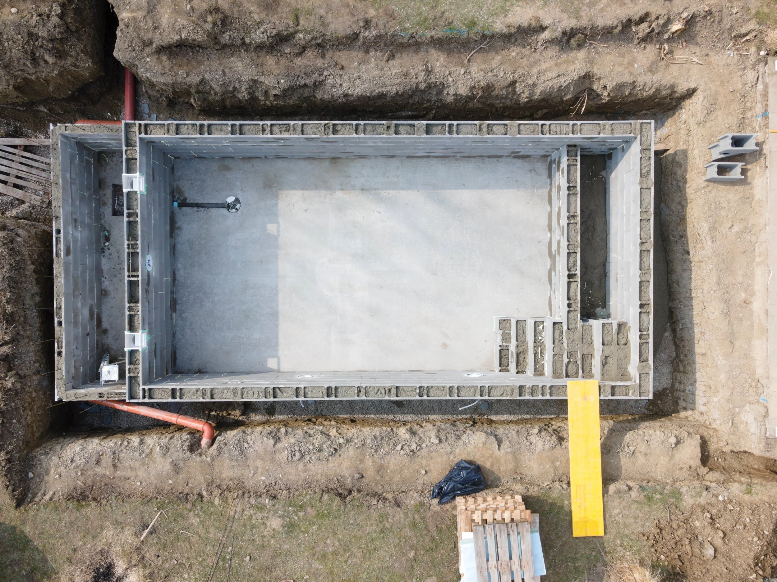 Construction site with new concrete foundation, cinder block walls, and exposed dirt surrounding the structure.