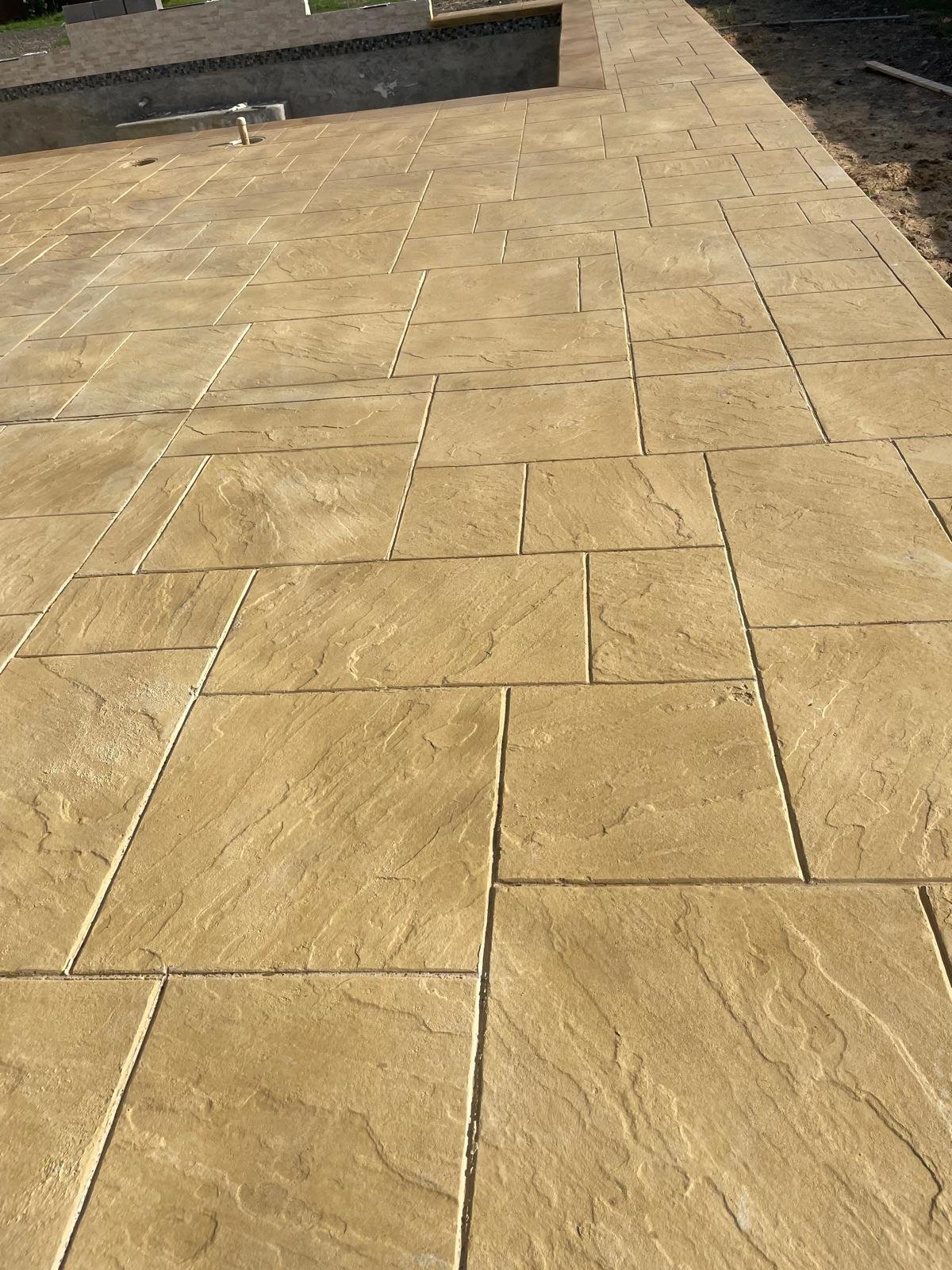 Close-up of a newly installed beige stone tile walkway with textured surface, arranged in a staggered pattern, extending into a construction site.