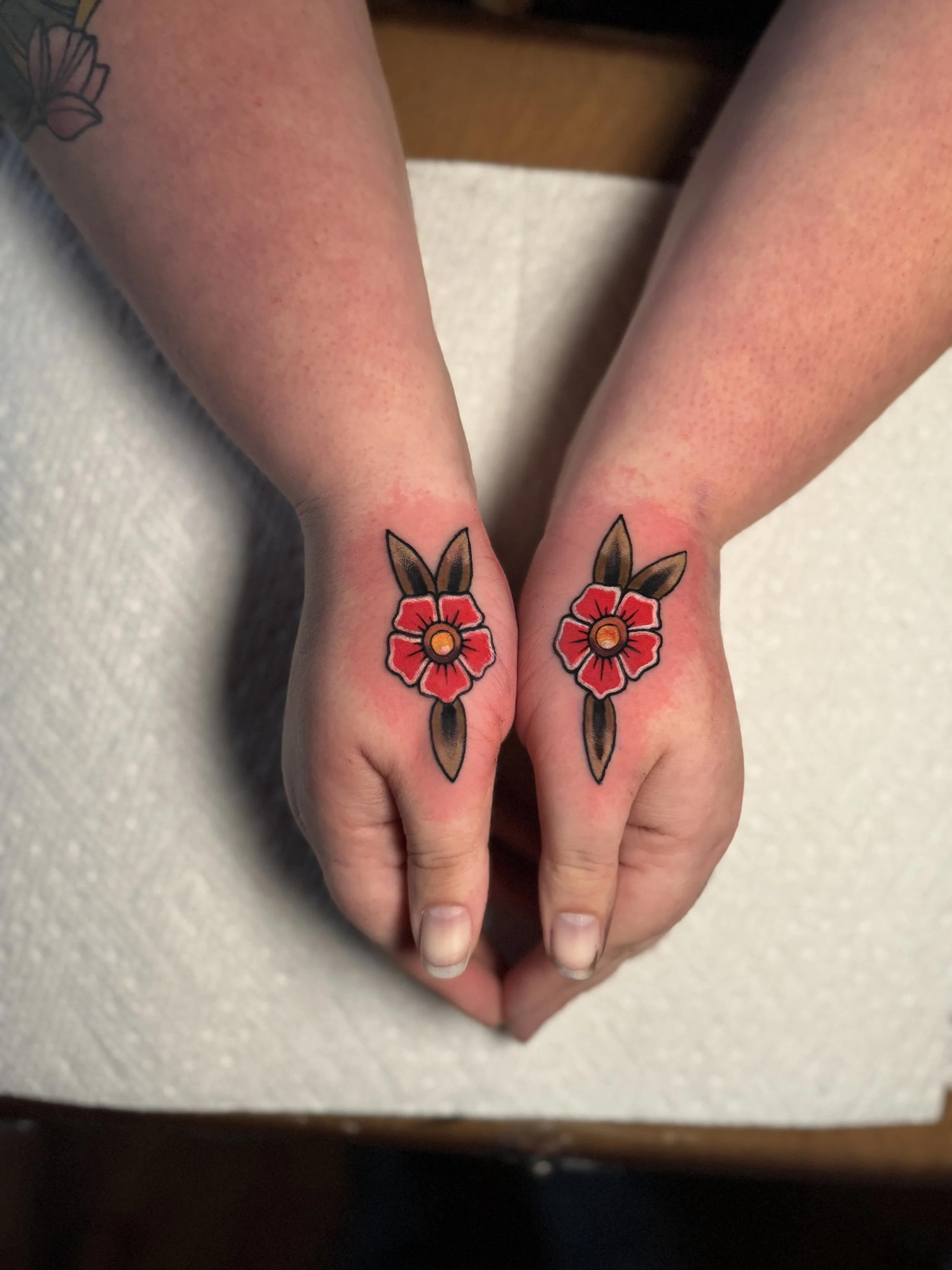 Close-up of hands with matching floral tattoos on the fingers, positioned to form a heart shape.