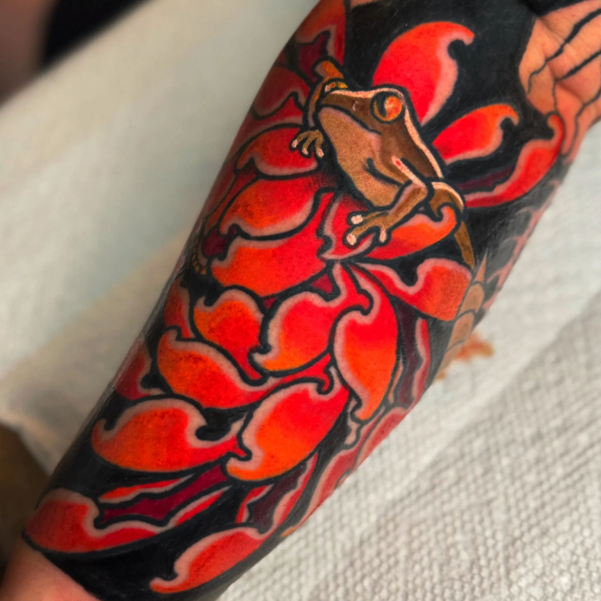 Close-up of a tattoo depicting a cartoonish animal, possibly a dragon or lizard, with a fiery red and orange background, outlined in black on skin.