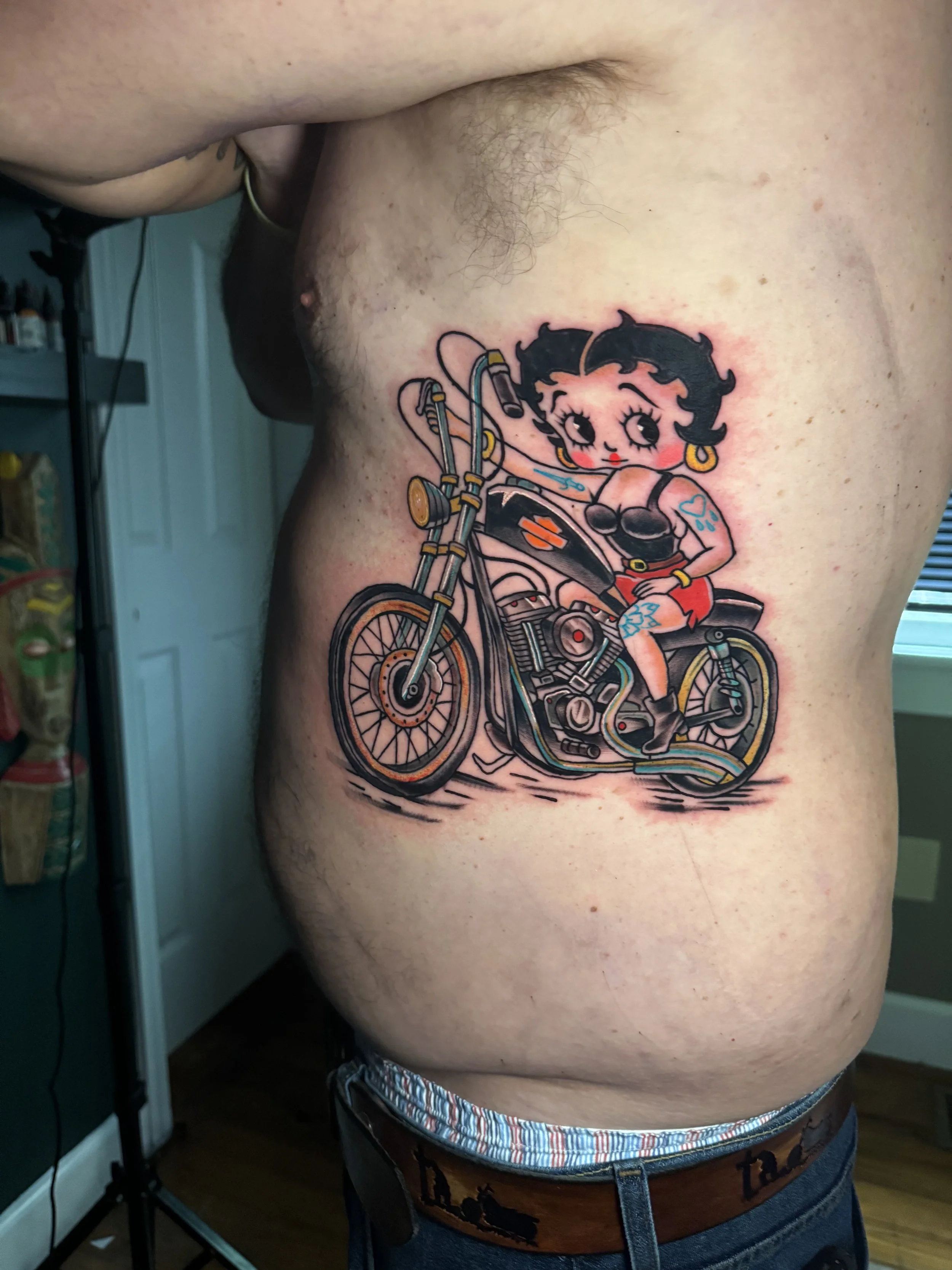 A tattoo of Betty Boop riding a motorcycle on a person's side.